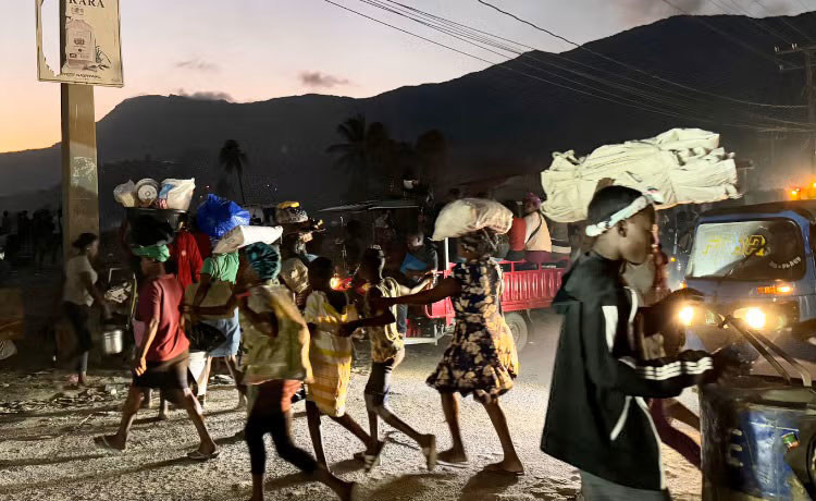 In Haiti, people carrying their belongings flee their homes at nightfall due to violence.