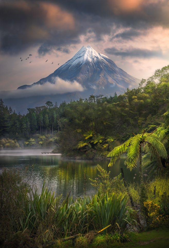 A snow-covered mountain with a tropical lake in the foreground