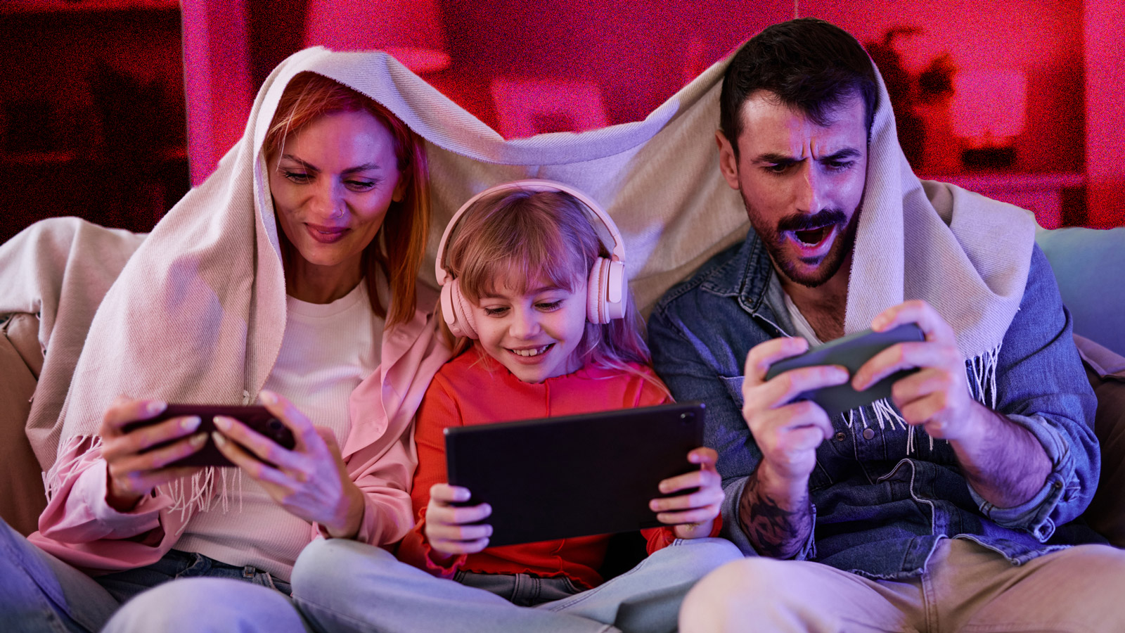 Young family sitting on the couch, all using phones and looking excited.