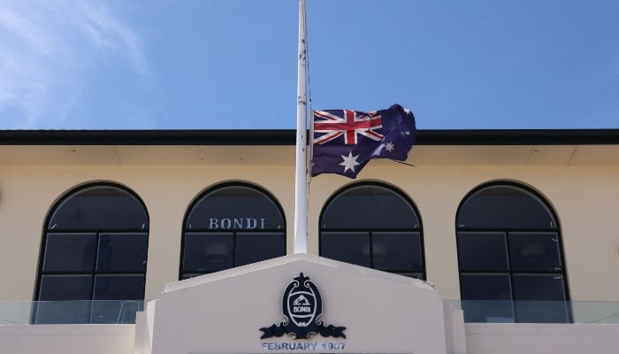 The Australian flag flies at half-mast at the Bondi Surf Bathers Life Saving Club, near the Bondi Beach boardwalk, where mourners left floral tributes to honor the victims of the shooting that took place there on December 14, in Sydney on December 18, 2025. — AFP
