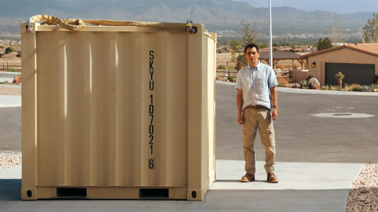 Manousos standing next to a giant steel box in episode 9 of Pluribus