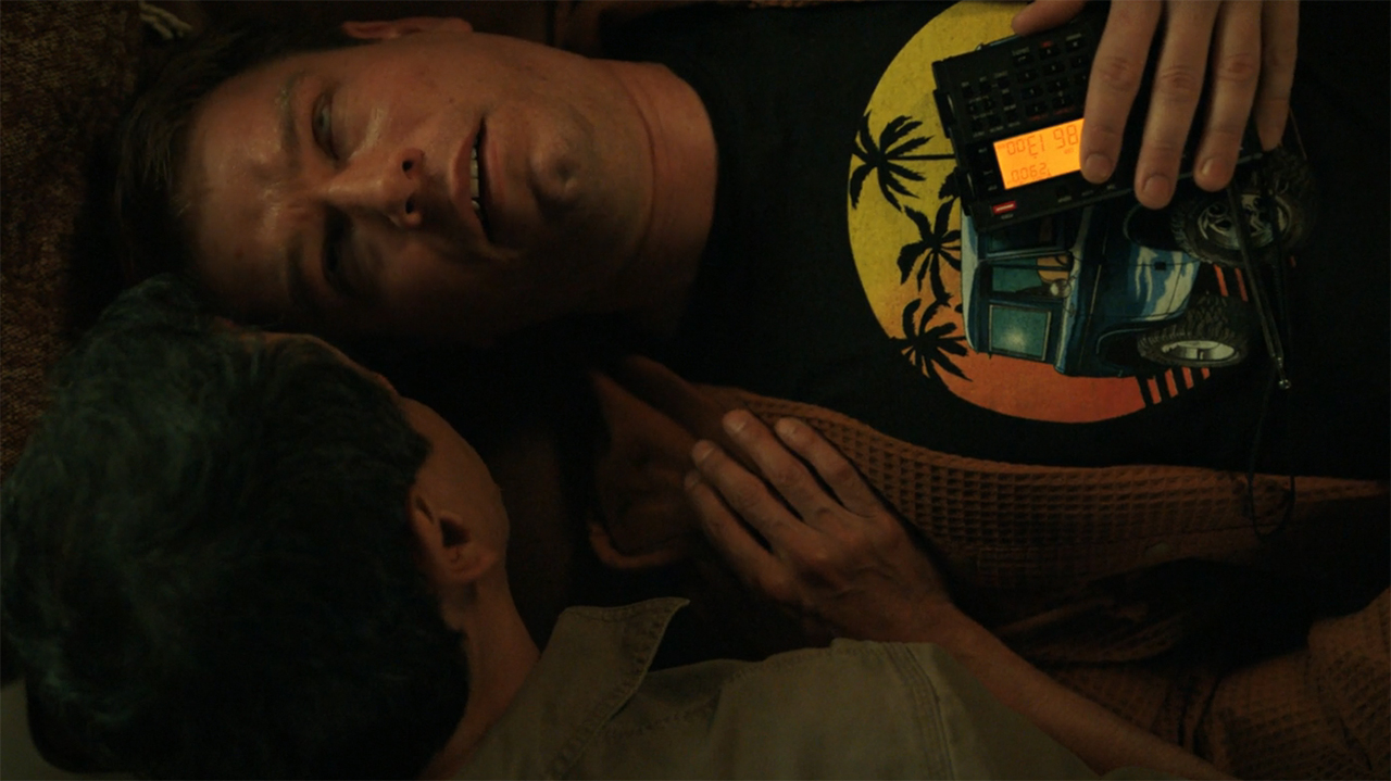 Manousos talking to a person with seizures with a portable radio on him in episode 9 of Pluribus