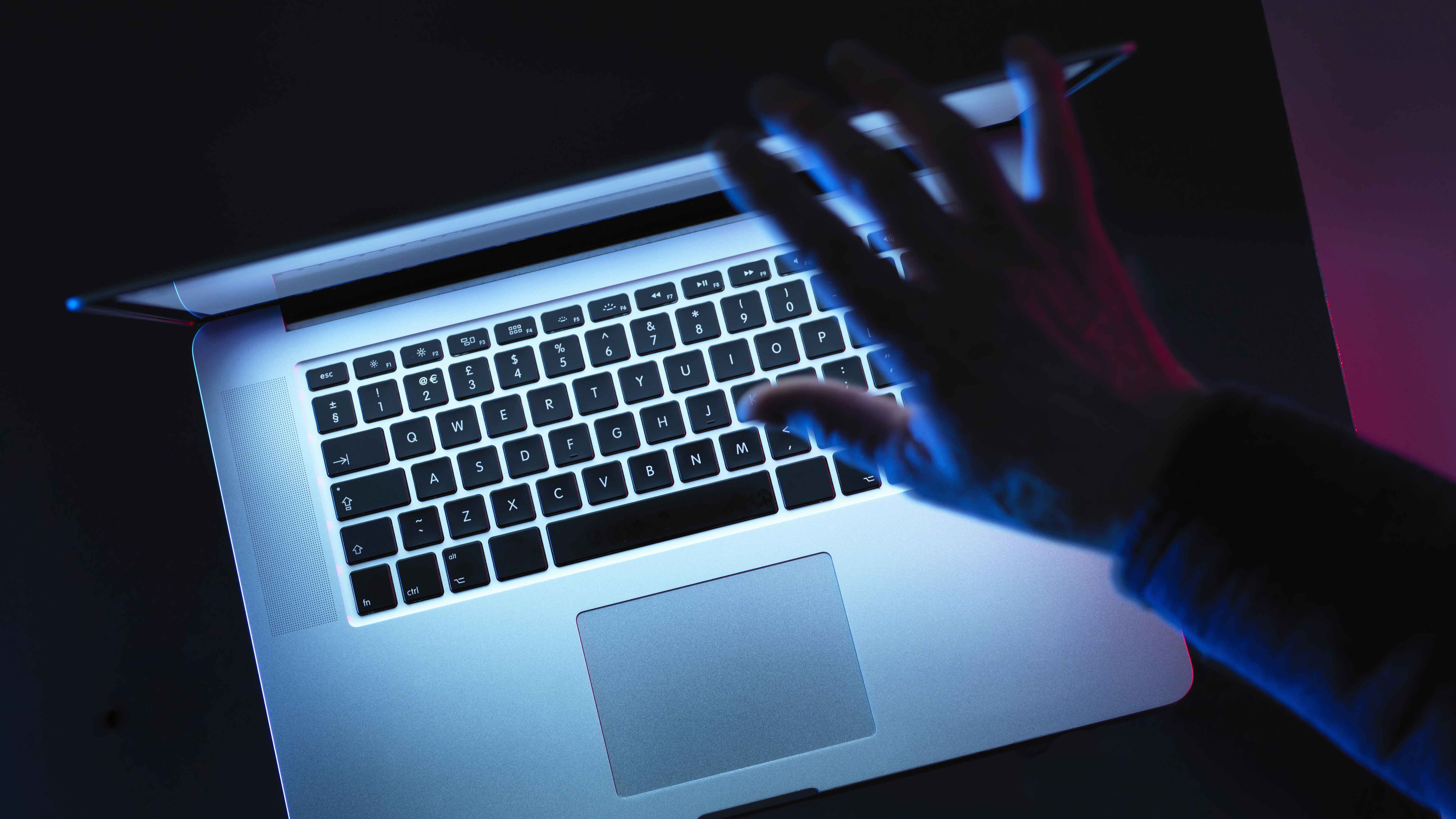 A hand closing a laptop screen in the dark.