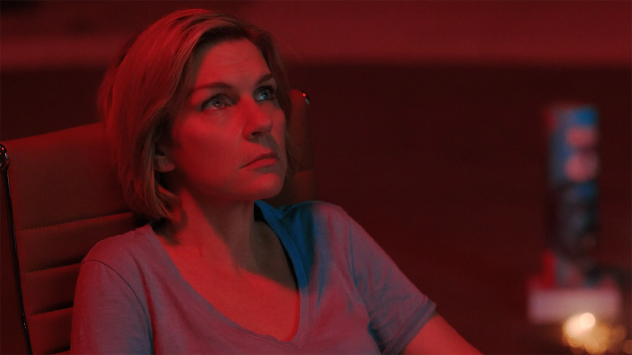 Carol sitting and bathed in the red light of a firework at night in episode 7 of Pluribus