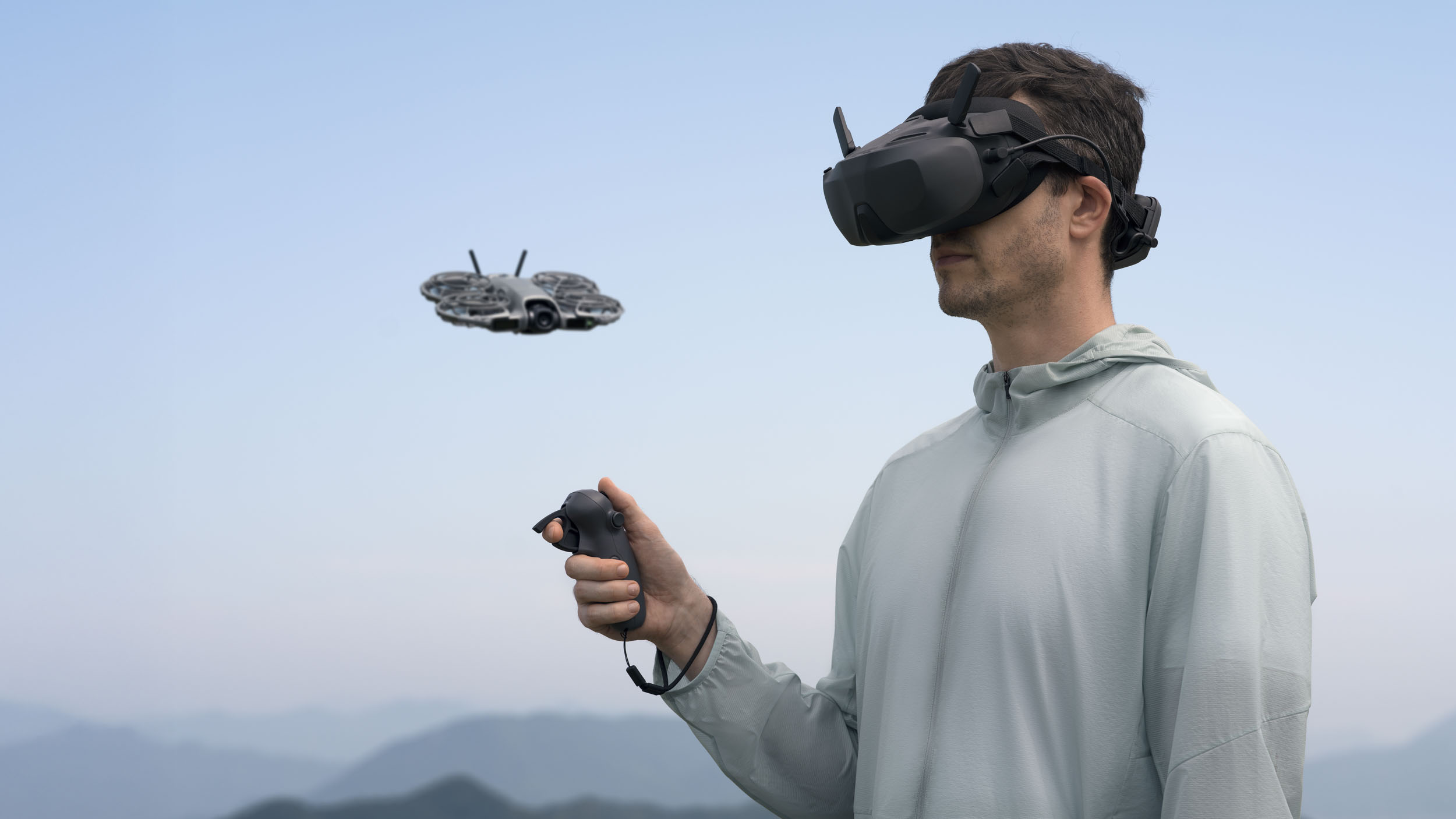 DJI Neo 2 selfie drone in flight next to a man wearing DJI glasses and holding a controller