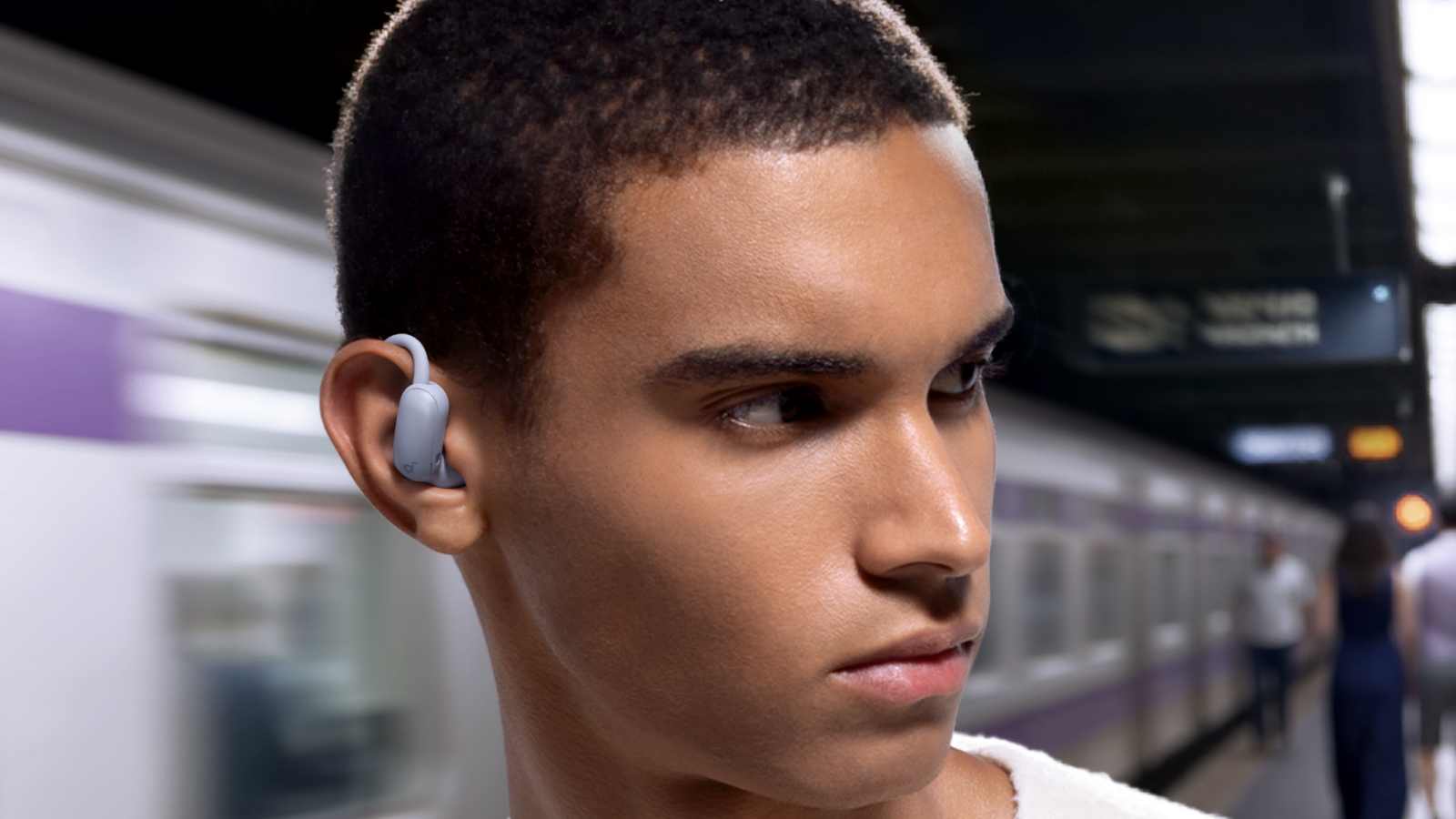 The Anker Soundcore Aerofit 2 Pro in a man's ear as he looks the wrong way while waiting for the train.