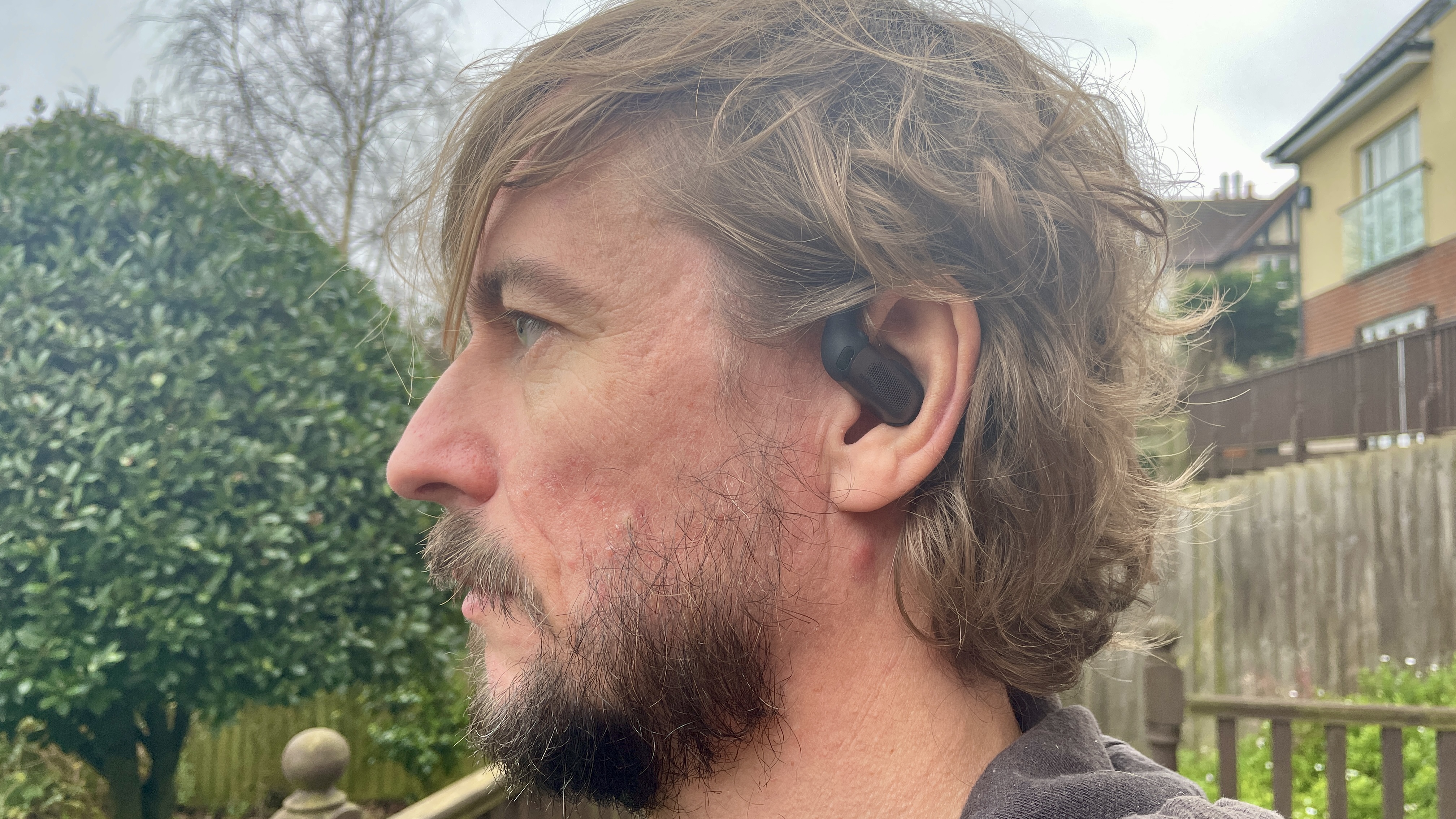 Shokz Openfit Pro outside, outside held in a woman's hand, with green grass in the background