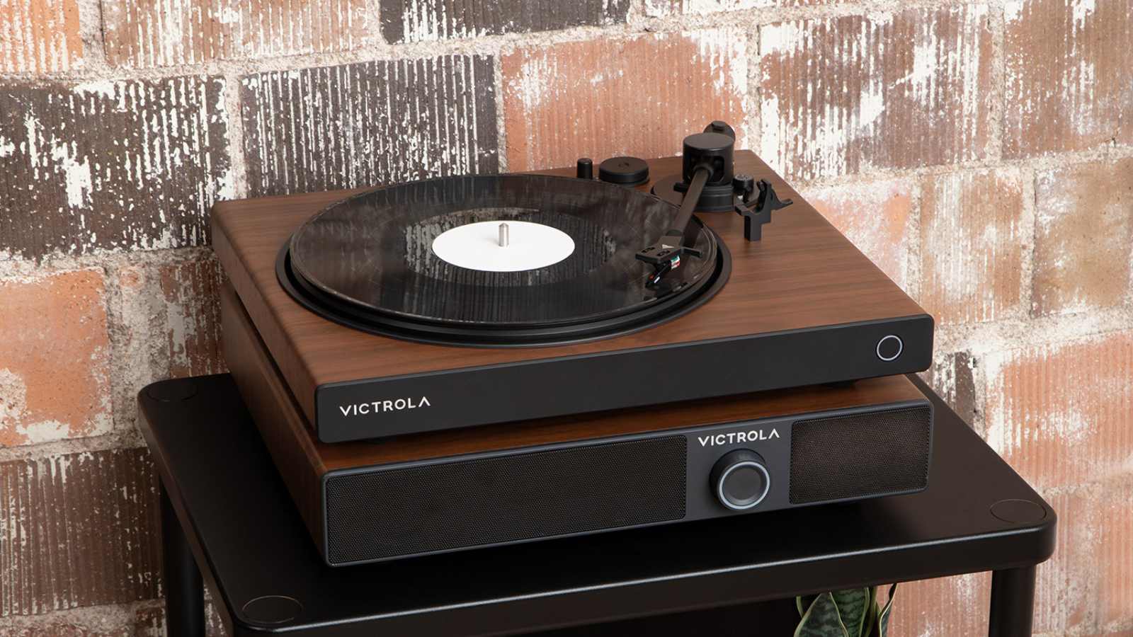 The Victrola Soundstage beneath a Victrola record player, on a table next to a brick wall.