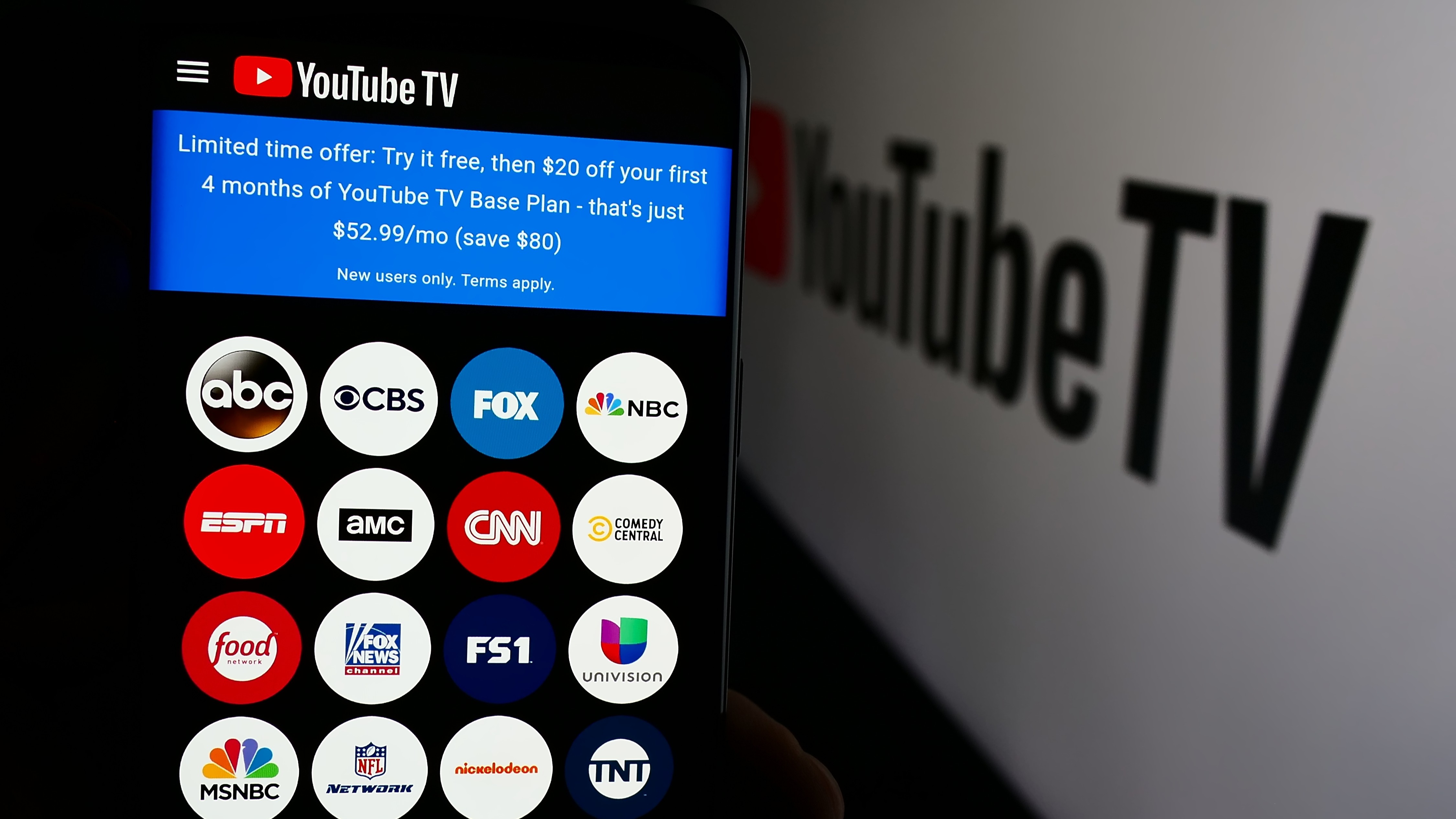 Person holding a cell phone with the YouTube TV web page in front of the company logo.