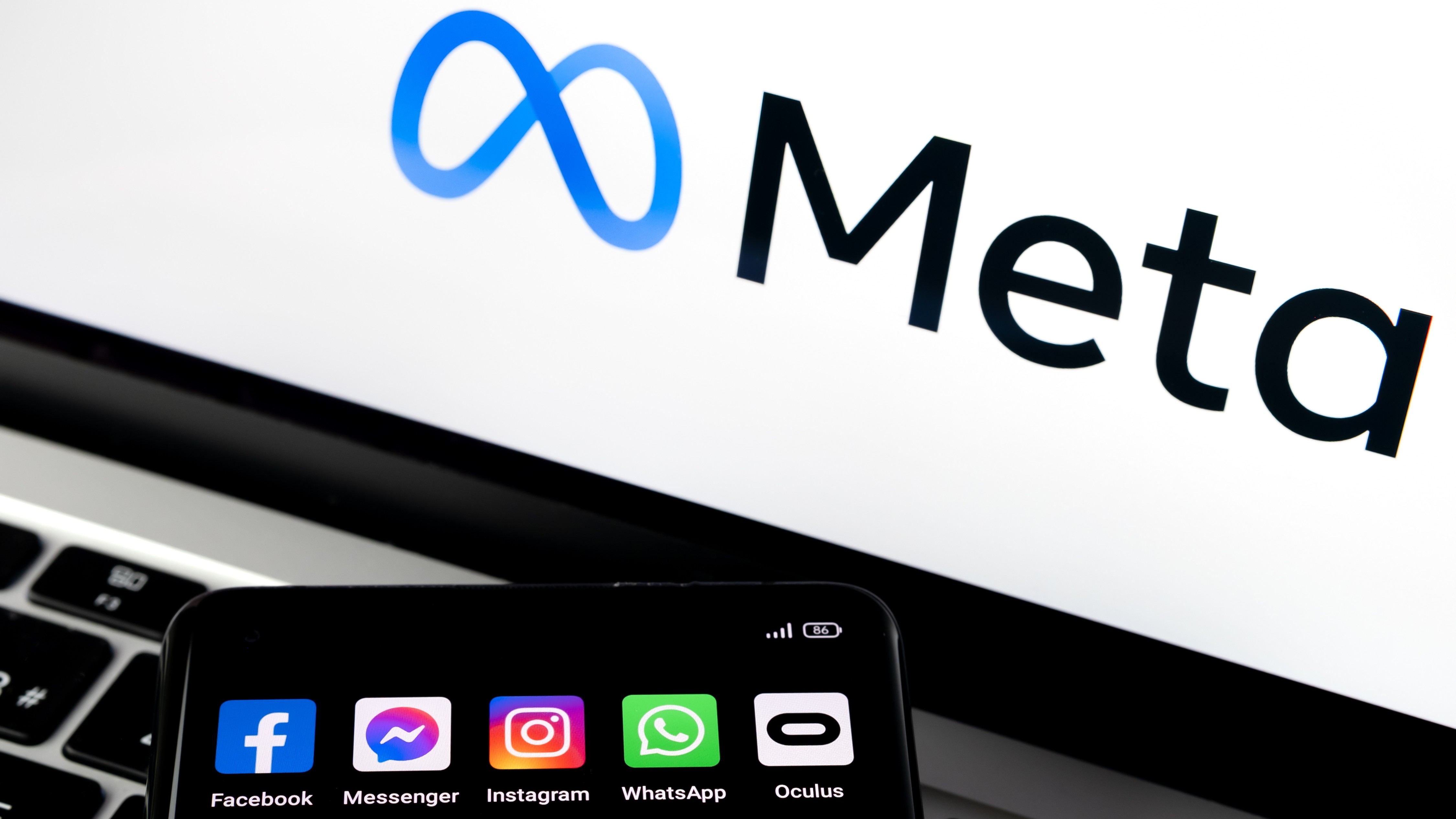 Smartphone silhouette with Facebook, Messenger, WhatsApp, Instagram, Oculus apps and blurred META logo in the background