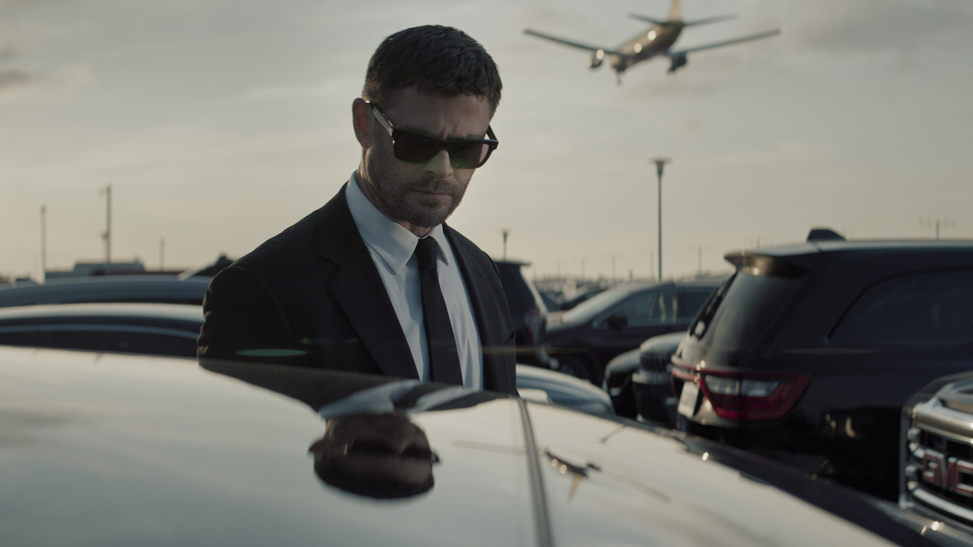 Mike Davis standing next to a car wearing sunglasses and a suit on Crime 101