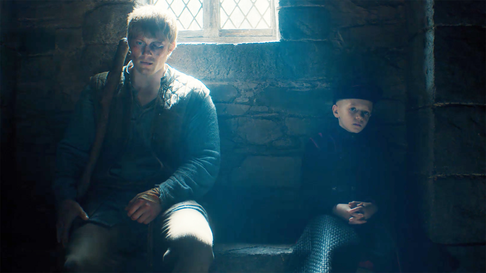 Dunk and Egg sitting on a bench inside a building as light comes in through a window in episode 6 of A Knight of the Seven Kingdoms.