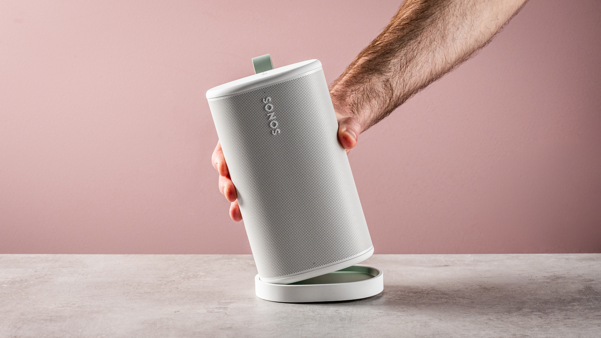 A man's hand removes the Sonos Play speaker from its charging base