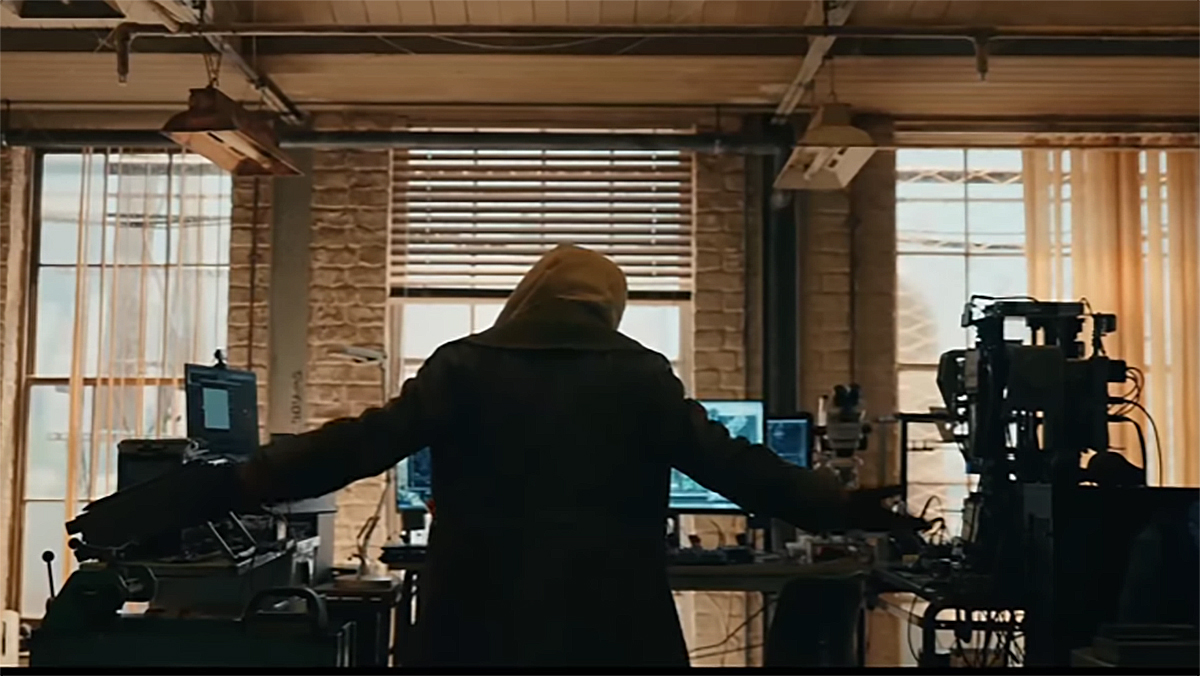 A hooded person slowly raises his hands while standing in front of a computer in Spider-Man: Brand New Day
