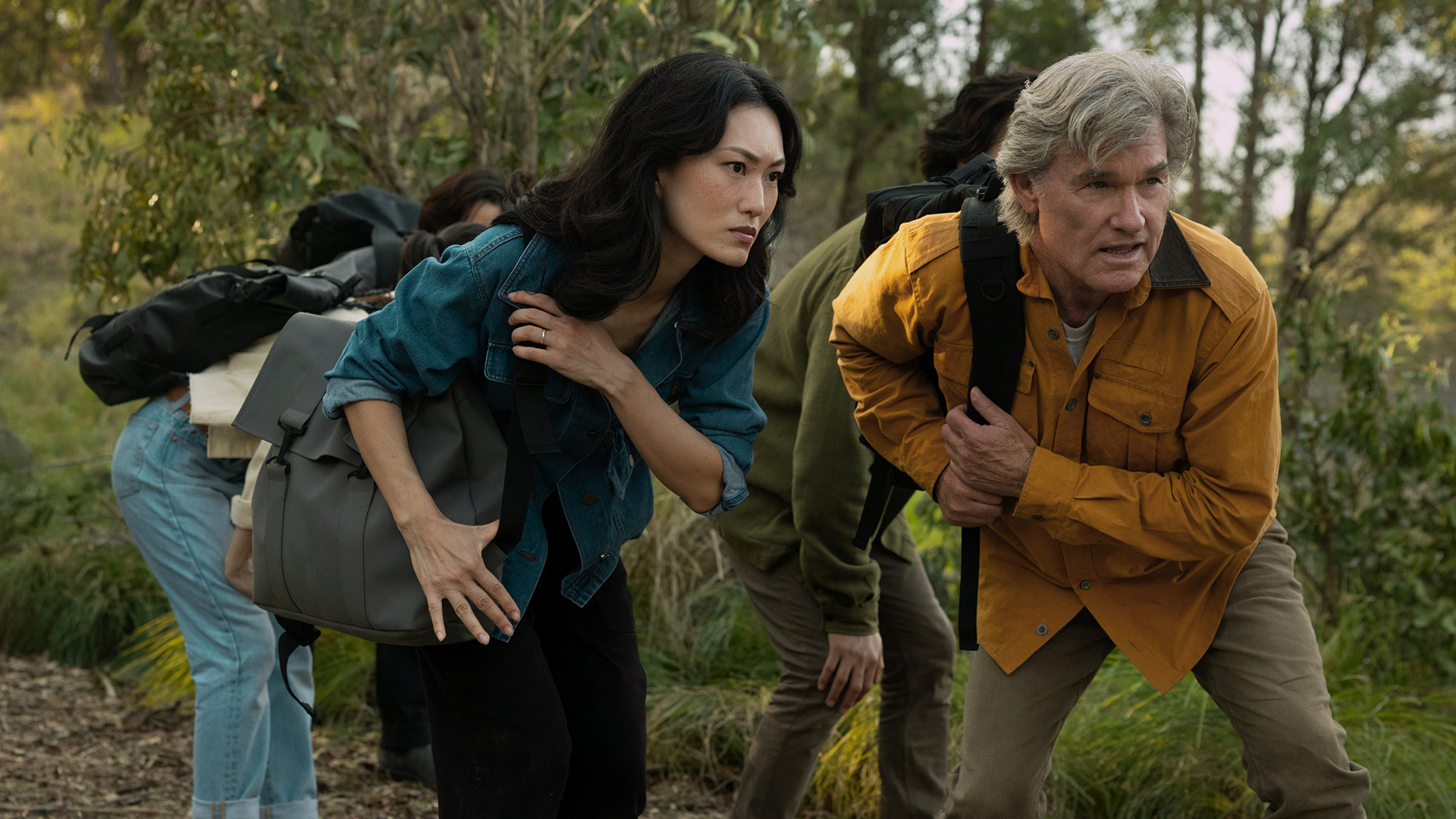 Keiko and Lee carrying backpacks and crouching in a forest in Monarch: Legacy of Monsters season 2 episode 5