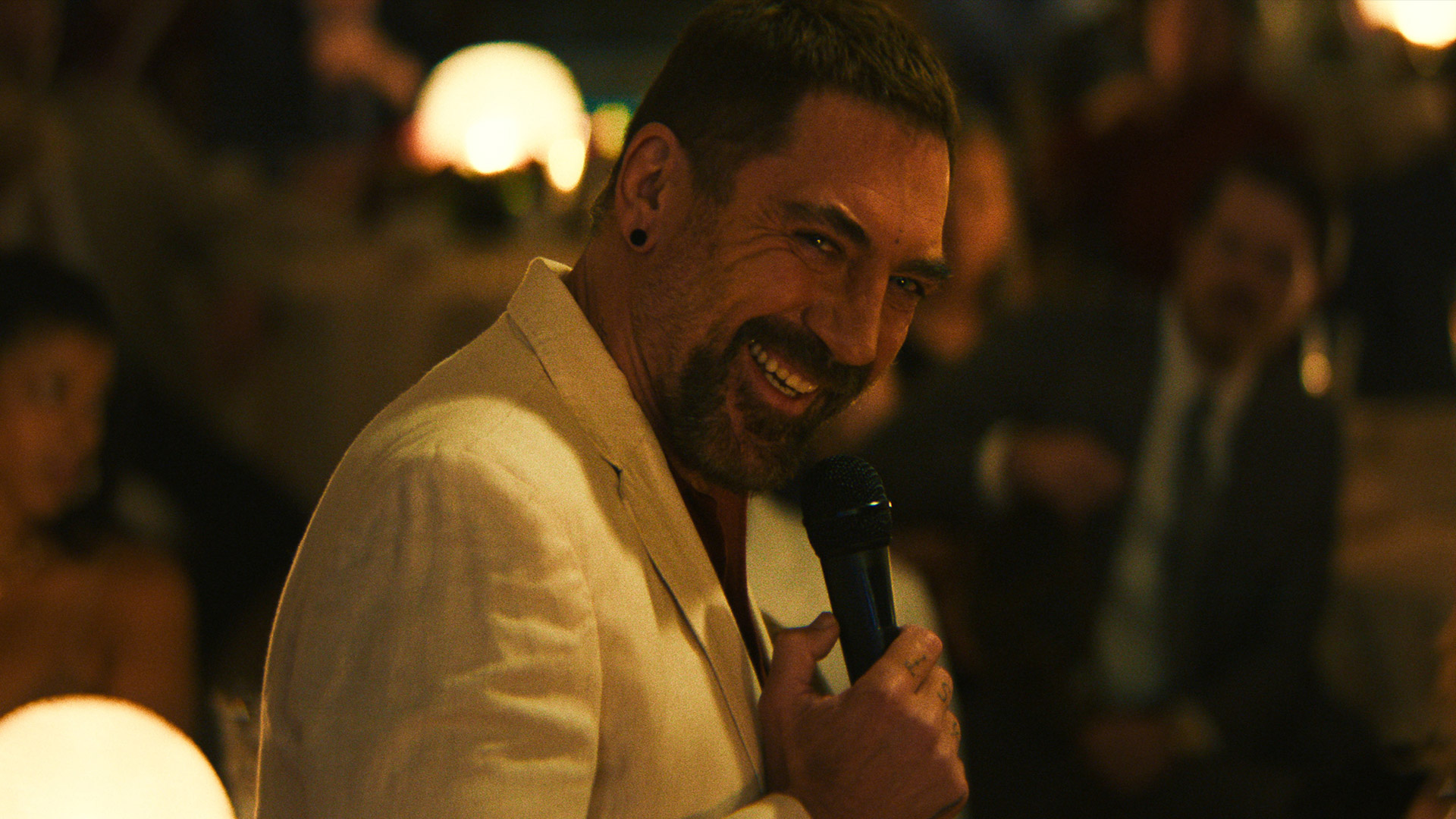 Javier Bardem smiles while holding a microphone as Max Cady in the Apple TV remake of Cape Fear