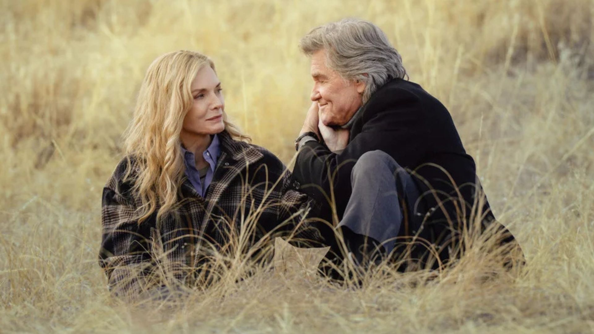 Michelle Pfeiffer and Kurt Russell sitting in the middle of a grass field