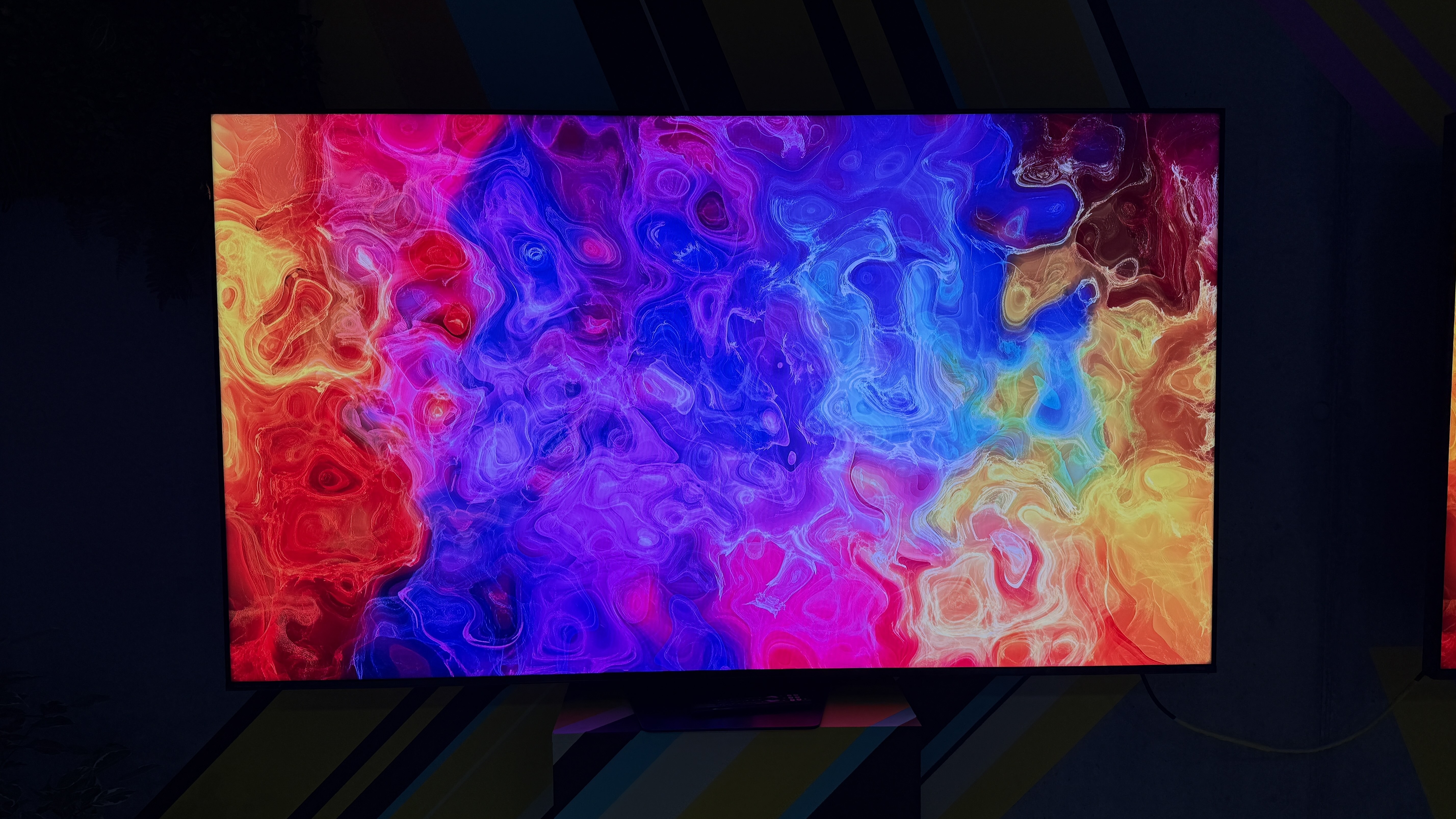 The Hisense UR9S RGB TV in a dark room, with an undulating color pattern on the screen showing off its impressive color reproduction