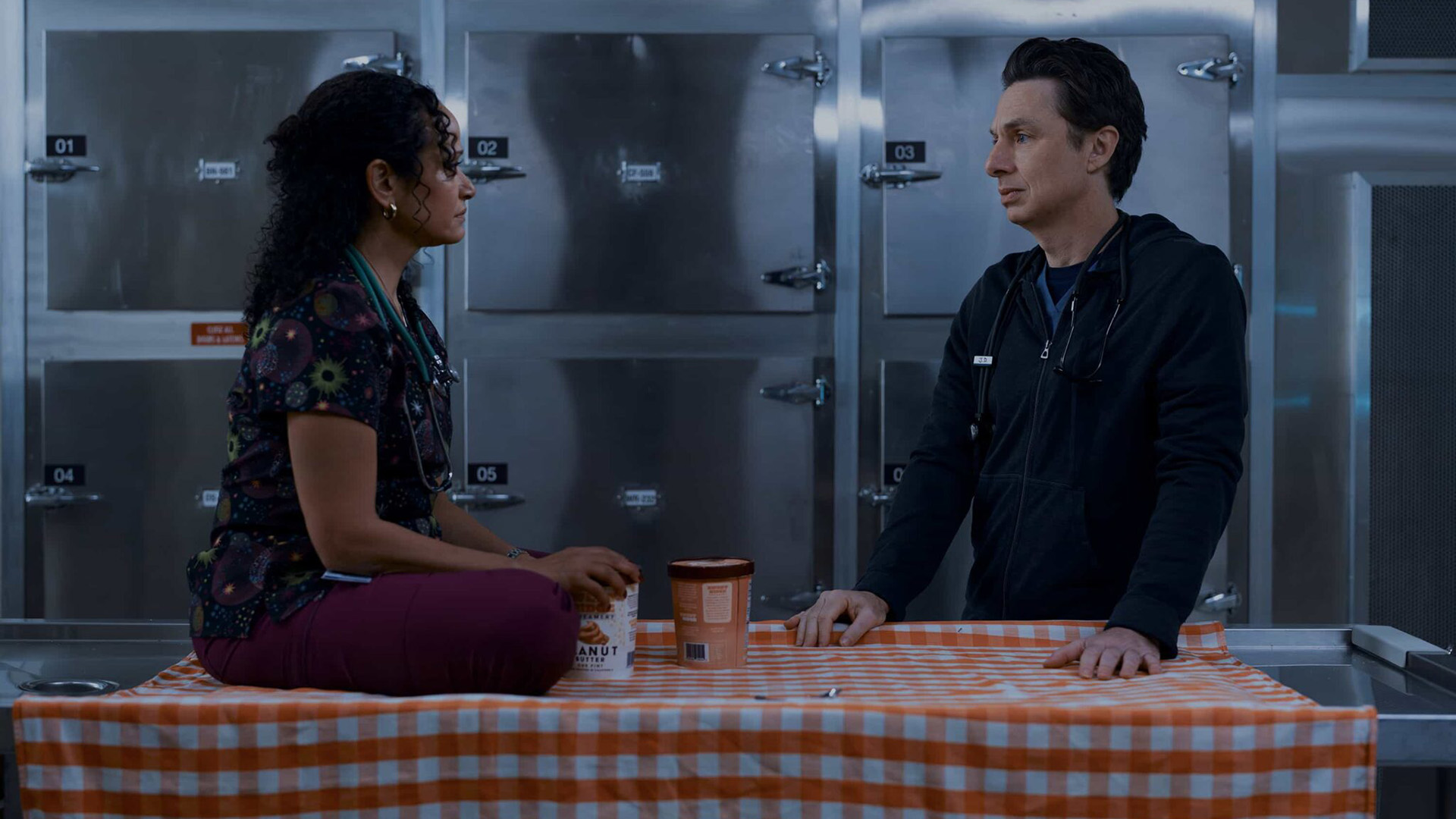 Carla sits cross-legged at a table next to the one JD is in in episode 7 of season 10 of Scrubs.