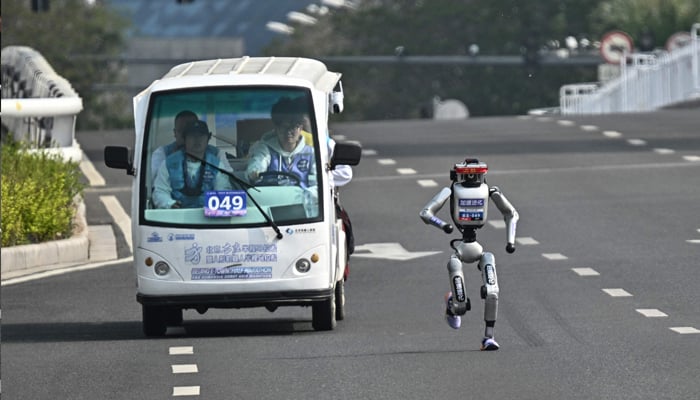 A robot and its engineers take part in the second Beijing E-Town Half Marathon and Humanoid Half Marathon in Beijing on April 19, 2026. — AFP