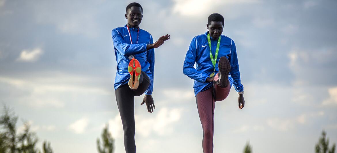 Two young African athletes in blue tracksuits stretch on a running track at the Teryet National High Altitude Training Center in Uganda. The image is part of a UNFPA documentation effort to highlight how athletics provides safe spaces and builds confidence in girls, particularly survivors of female genital mutilation (FGM).