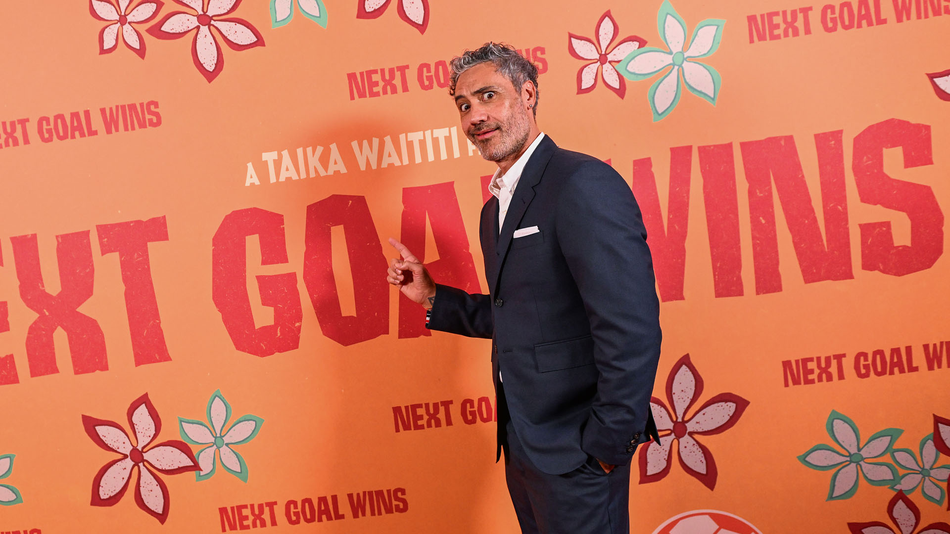 Taika Waititi makes a face while pointing at the Next Goal Wins movie logo during the film's premiere.