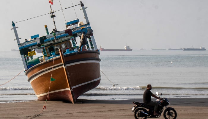 In this image obtained from the Iranian news agency ISNA on April 24, 2026, an Iranian man rides his motorcycle past a boat on Suru Beach in Bandar Abbas, along the Strait of Hormuz. —AFP