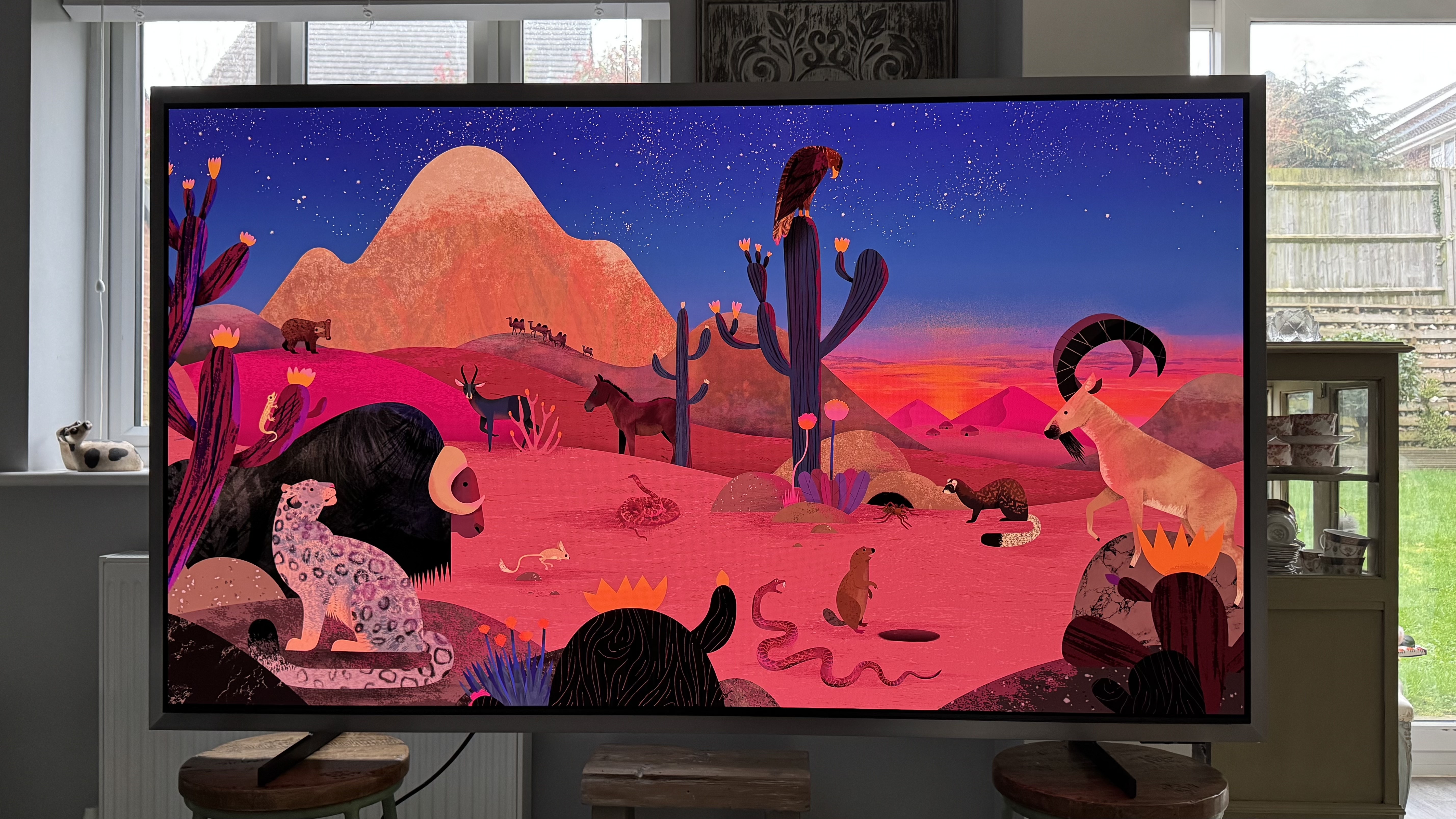 The Samsung S99H/S95H TV in a home, showing an abstract image of a desert scene on the screen, showing off its striking colors.