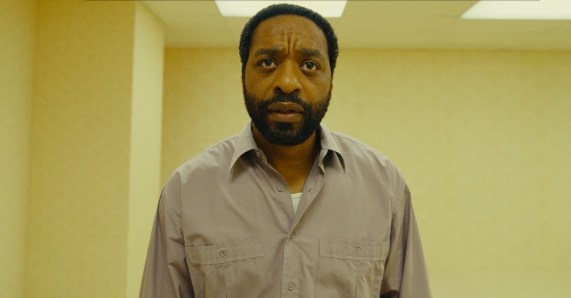 Chiwetel Ejiofor standing in Backrooms, where he is surrounded by pale yellow walls and fluorescent lights.