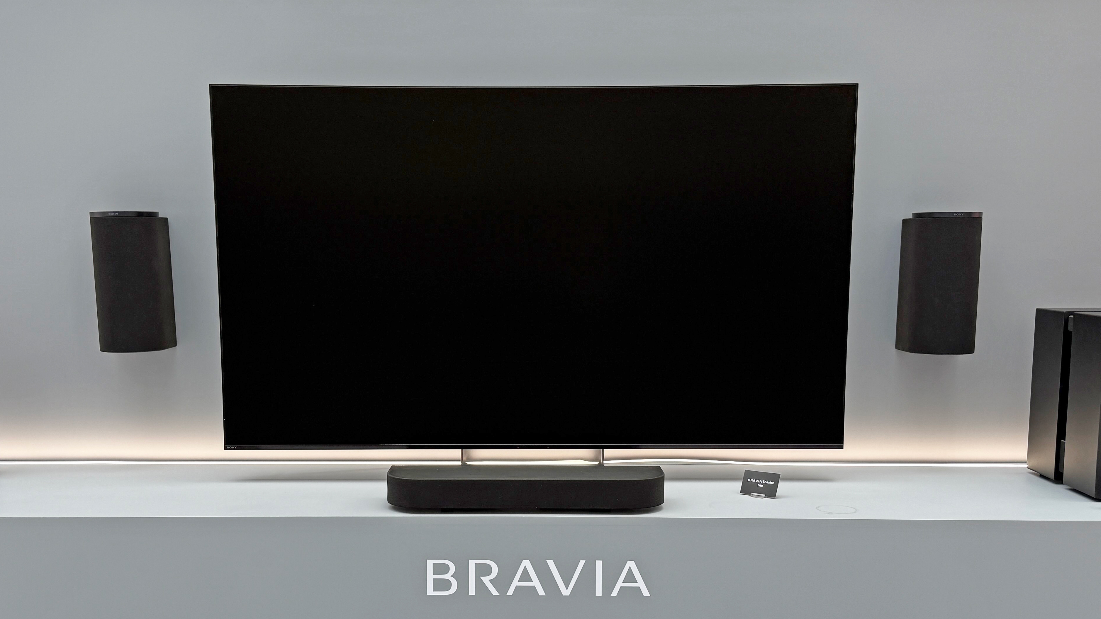 The Sony Bravia Theater Trio with a black television screen. Two speakers are hanging on the wall, on either side of a television with a small speaker below