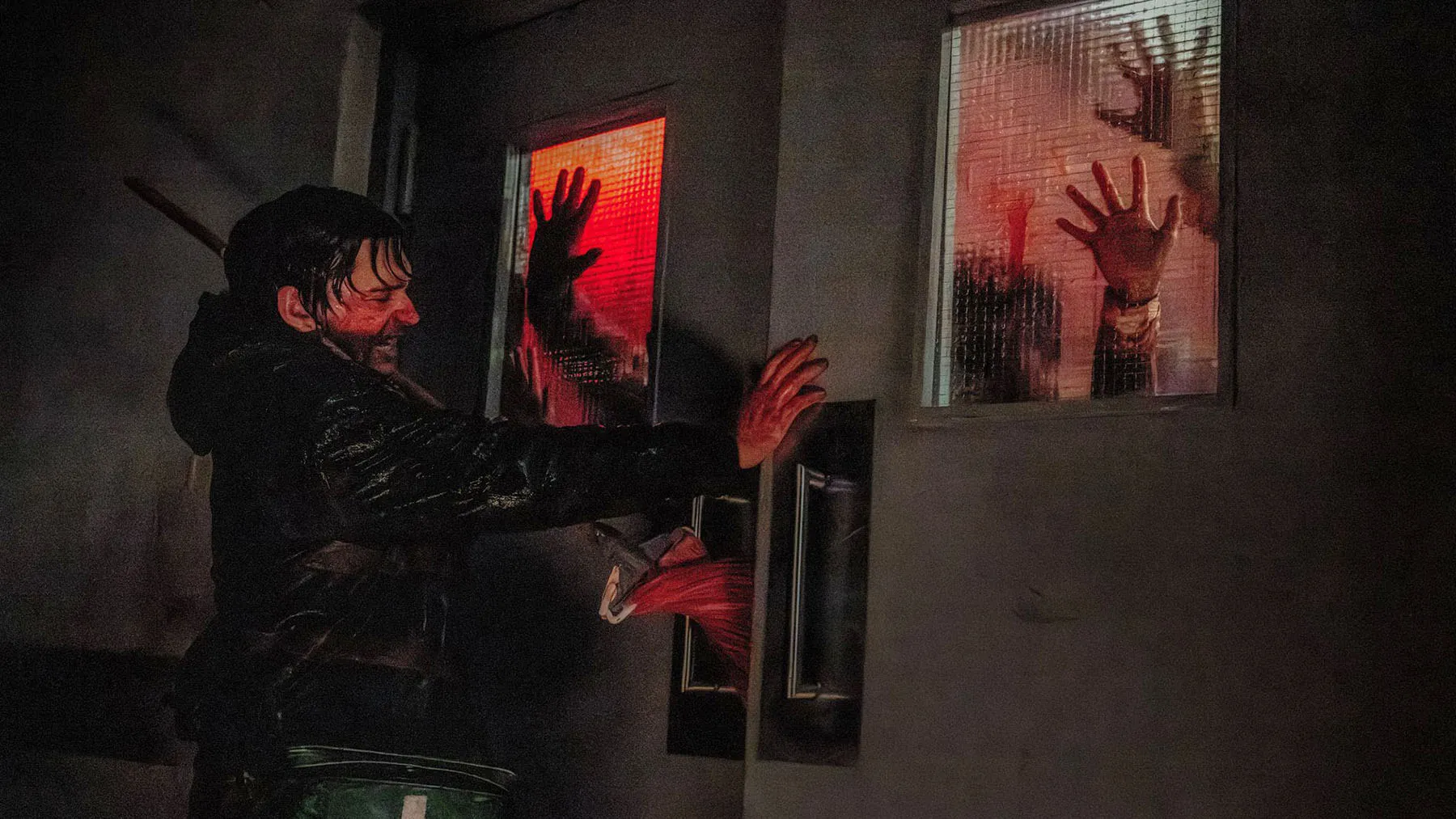 A man barricades himself behind a door while bloody handprints are seen on the other side.