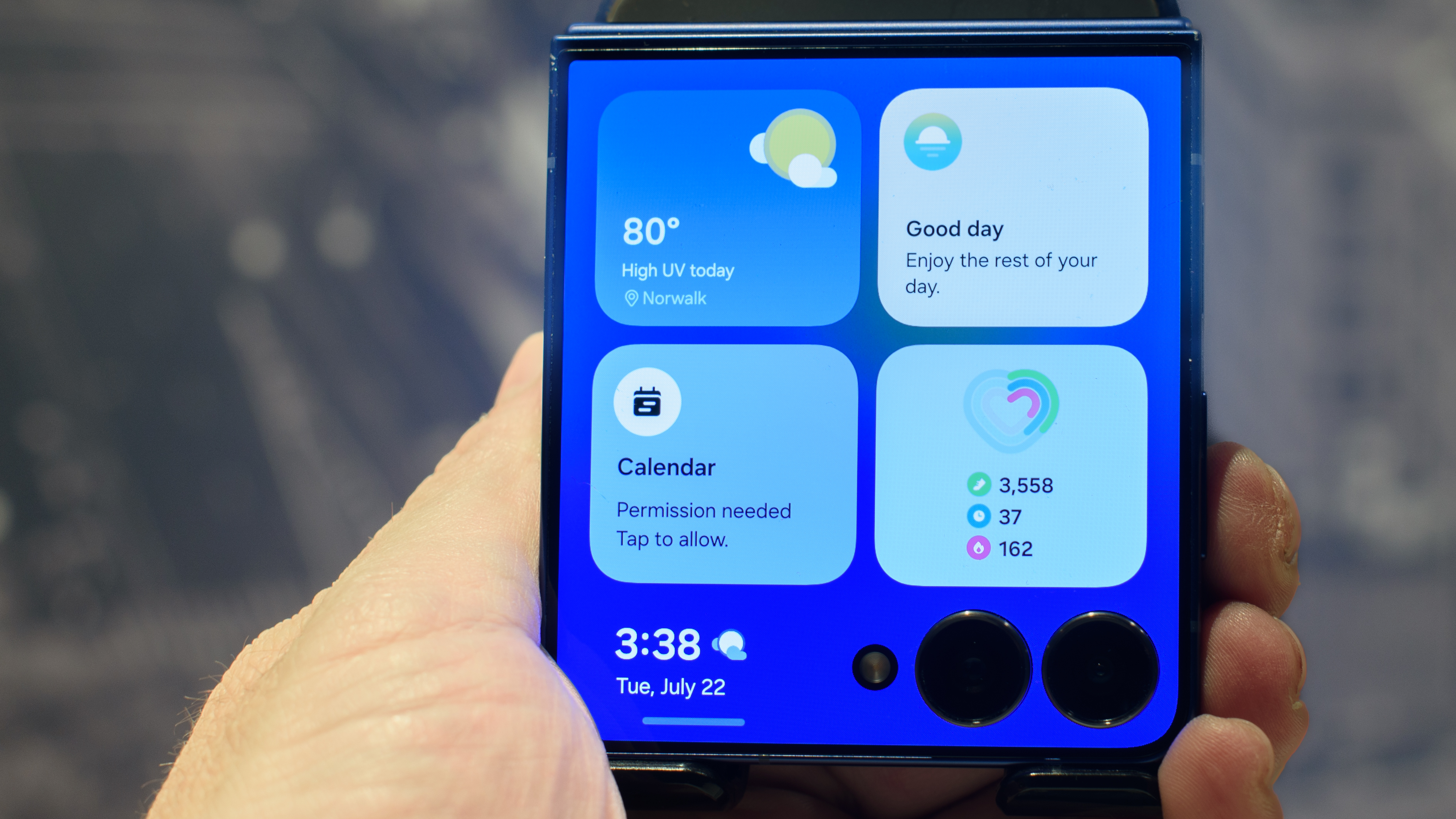 Samsung Galaxy Z Flip 7 in blue in hand showing four widgets on the cover screen including weather, now brief, calendar and health monitor.