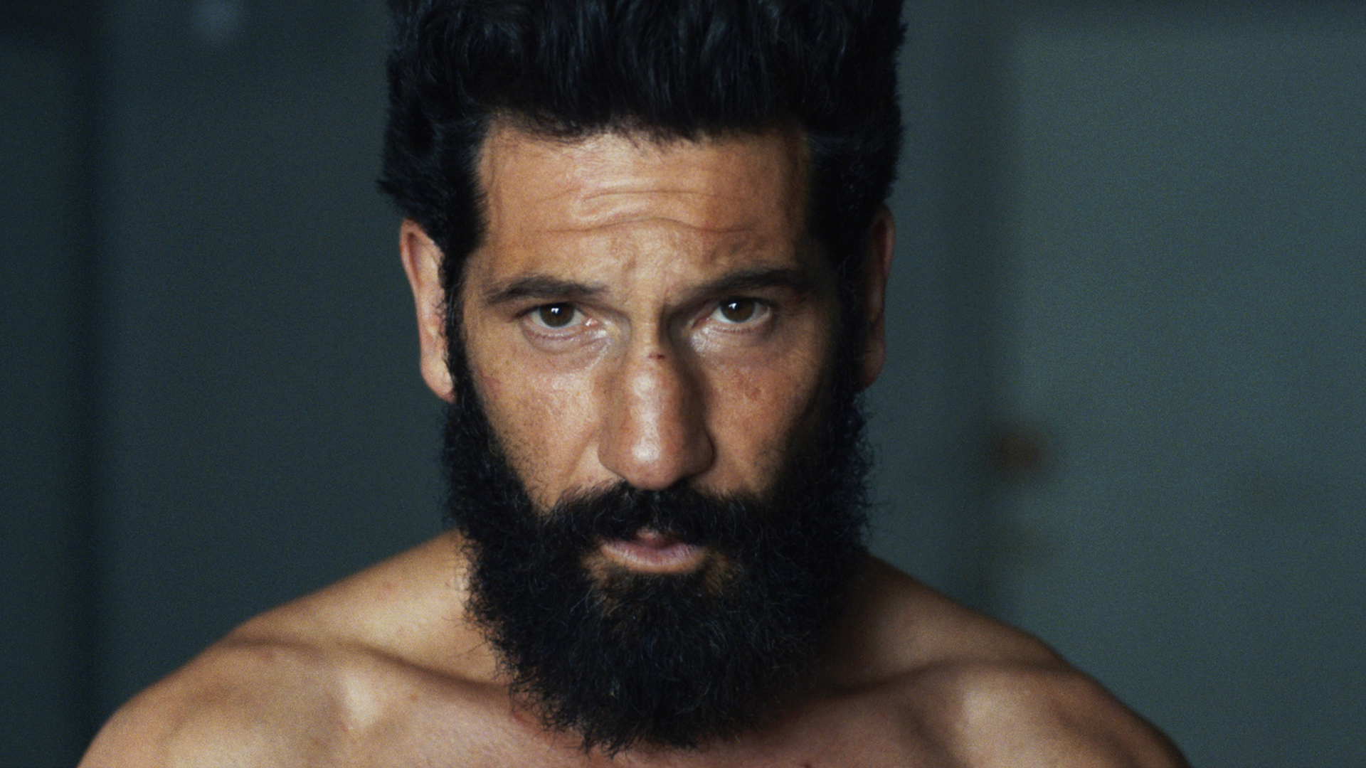 Head and shoulders image of Jon Bernthal's Frank Castle with a beard, shirtless and looking at the camera in The Punisher: One Last Kill.