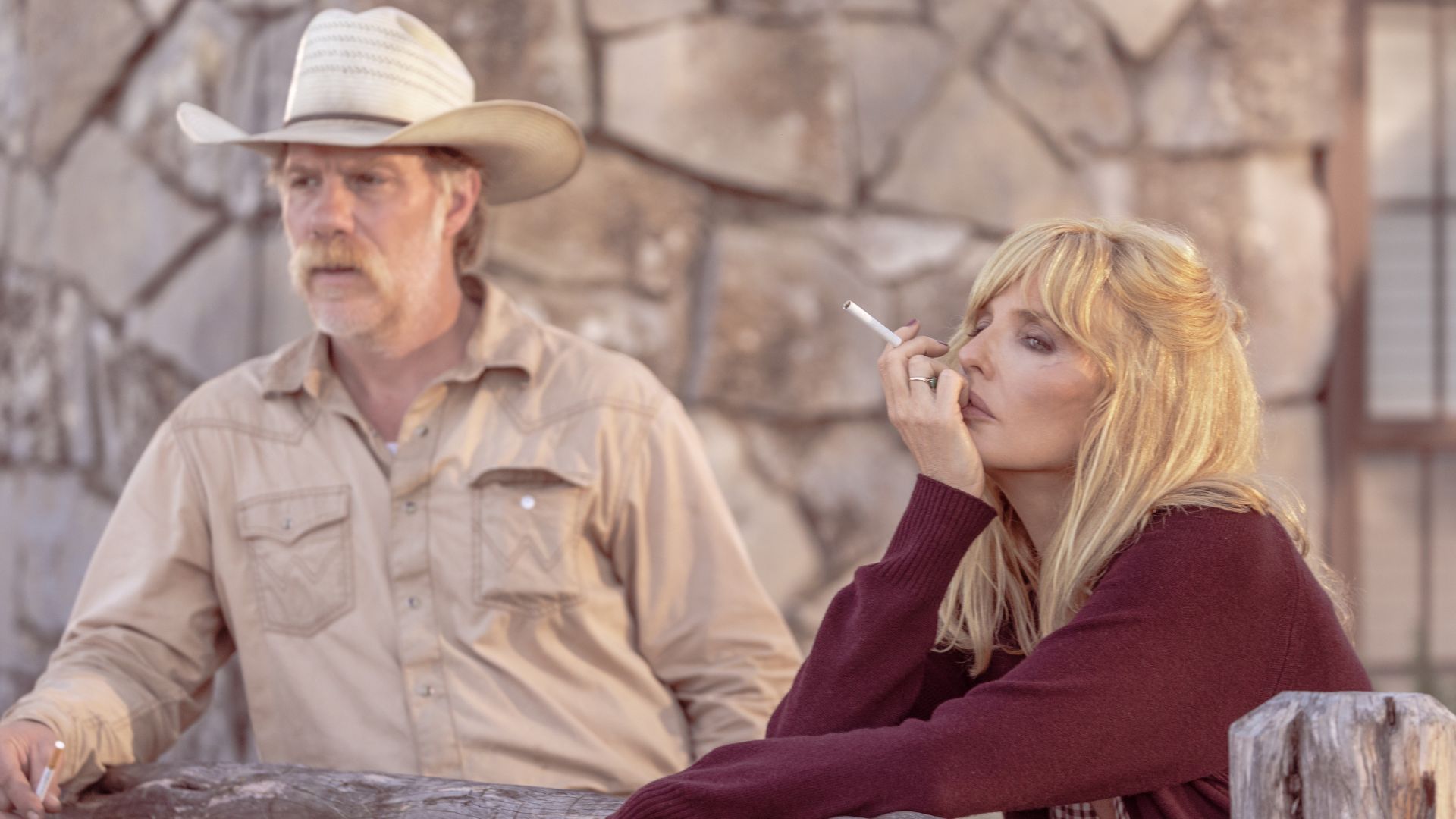 Beth smokes while leaning on a wooden fence with Zachariah behind