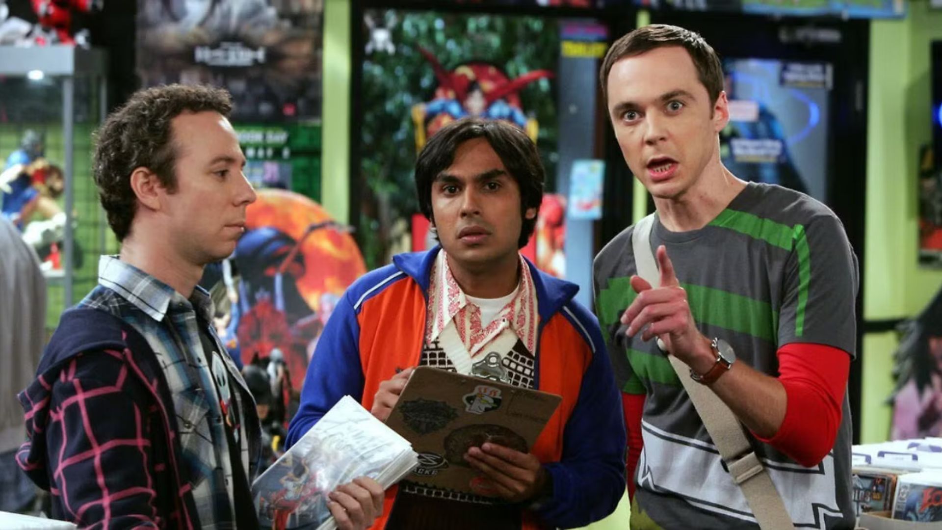Sheldon points at something off-screen as Raj stares, with Stuart staring straight into space.