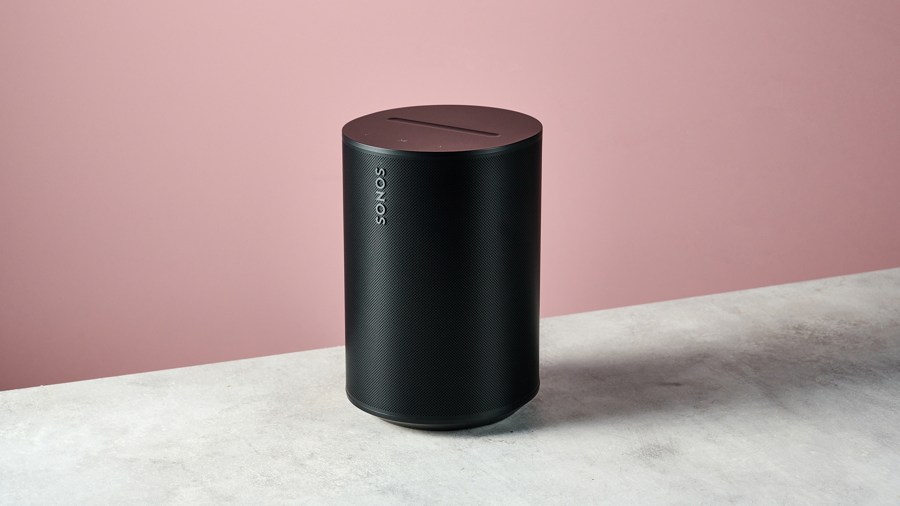The Sonos Era 100 SL at a 3/4 angle in front of a pink background.