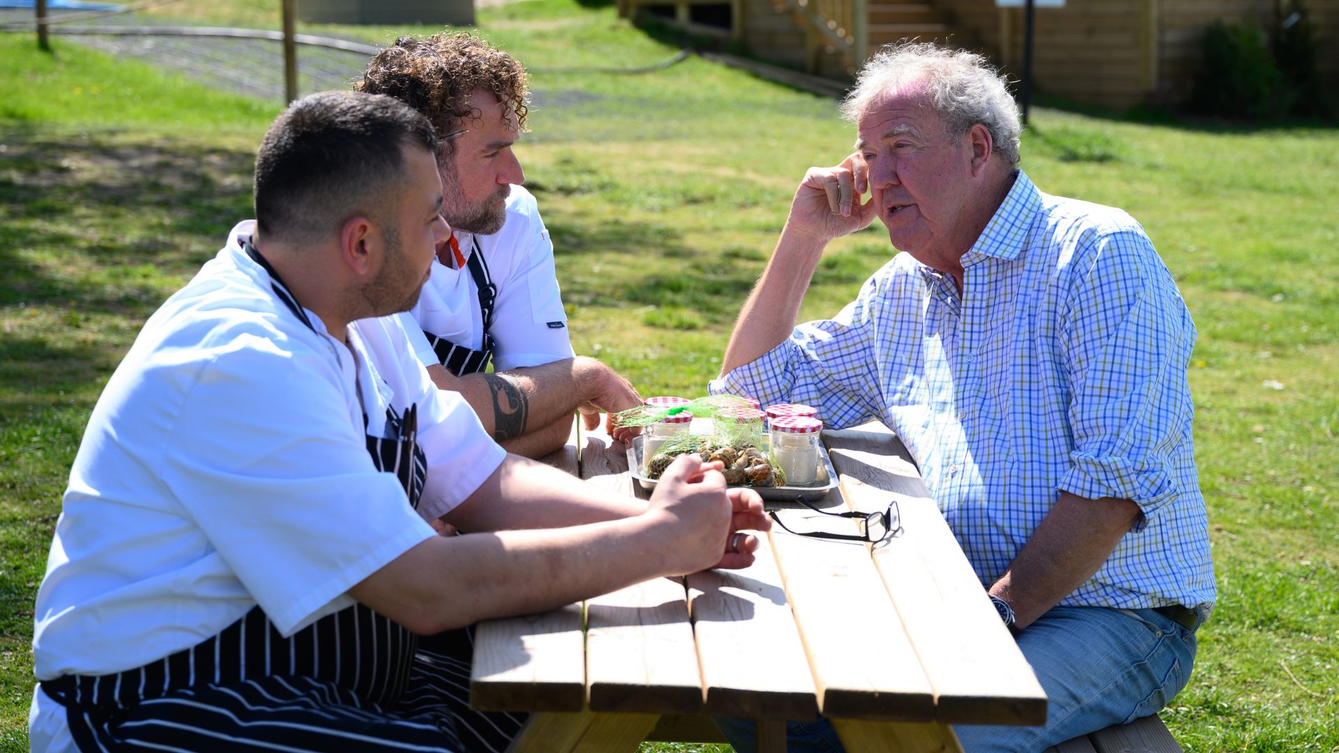 Jeremy talks to two chefs sitting at a picnic table.