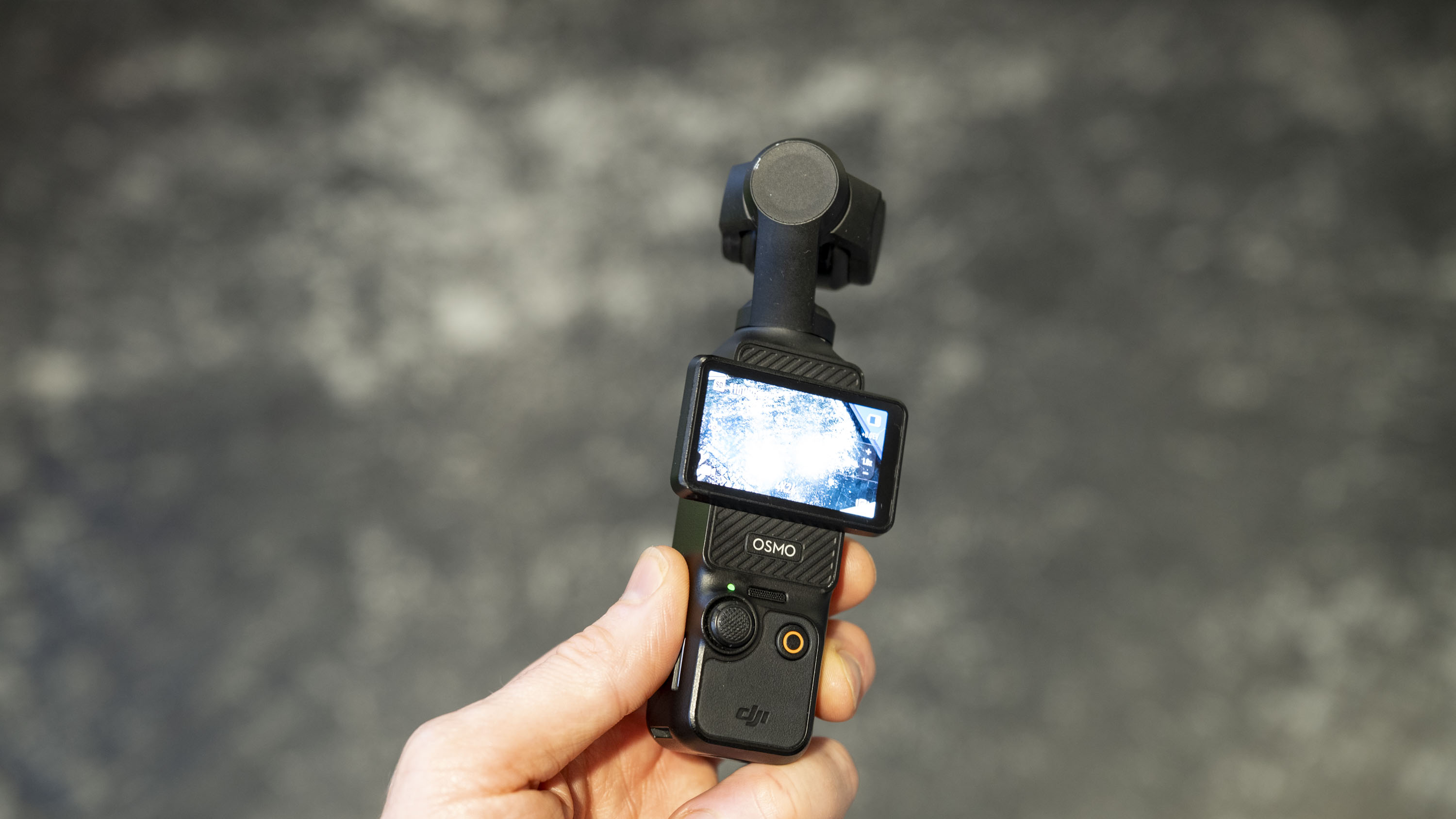 DJI Osmo Pocket 3 vlogging camera in user's hand, gray floor in the background