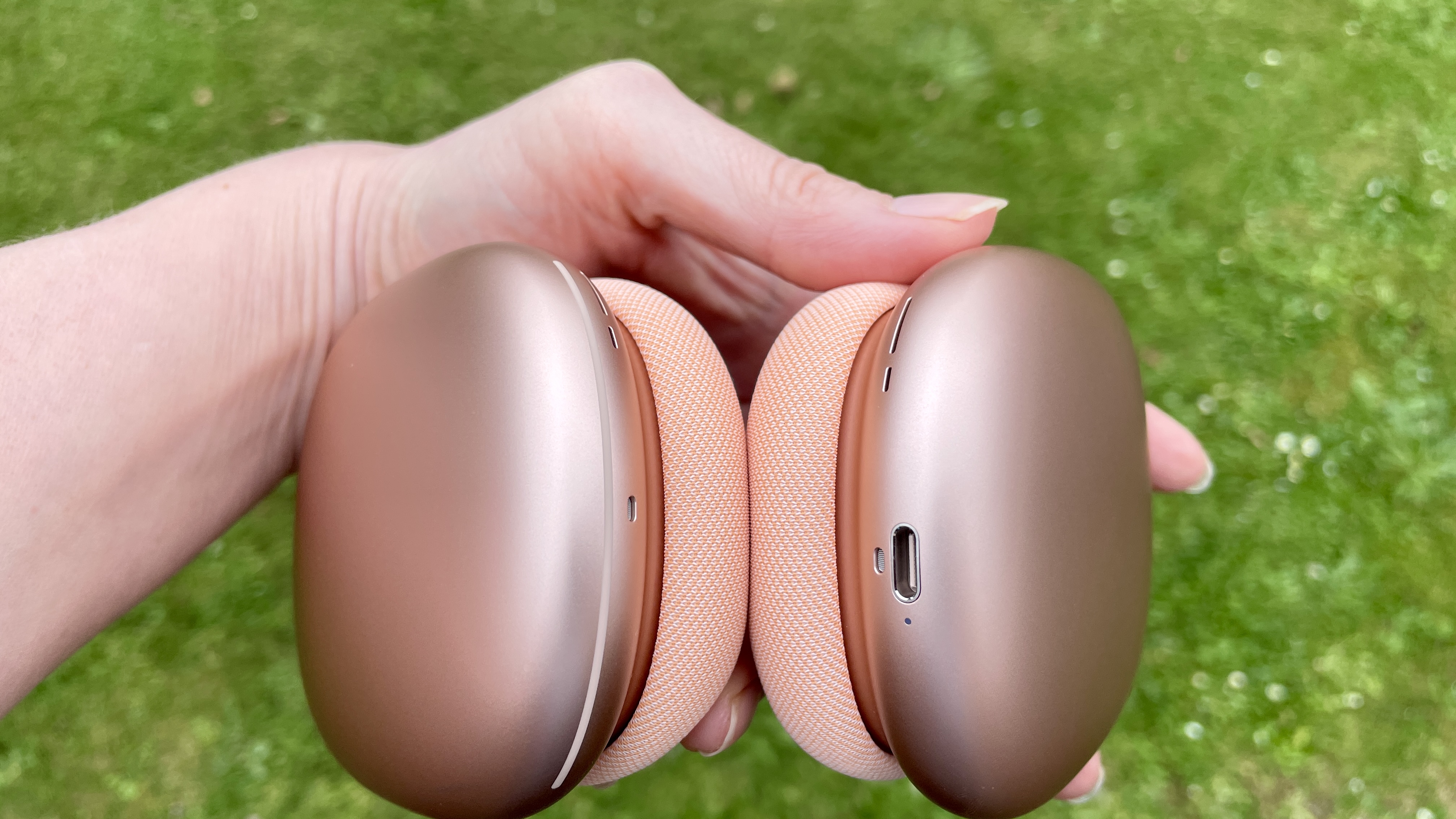 AirPods Max 2 in a garden, held in one hand, close-up to show the earbuds and band