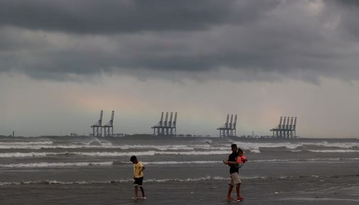 Children play, with rainbows and rain clouds in the background, at Clifton Beach in Karachi, on August 30, 2024. – Reuters