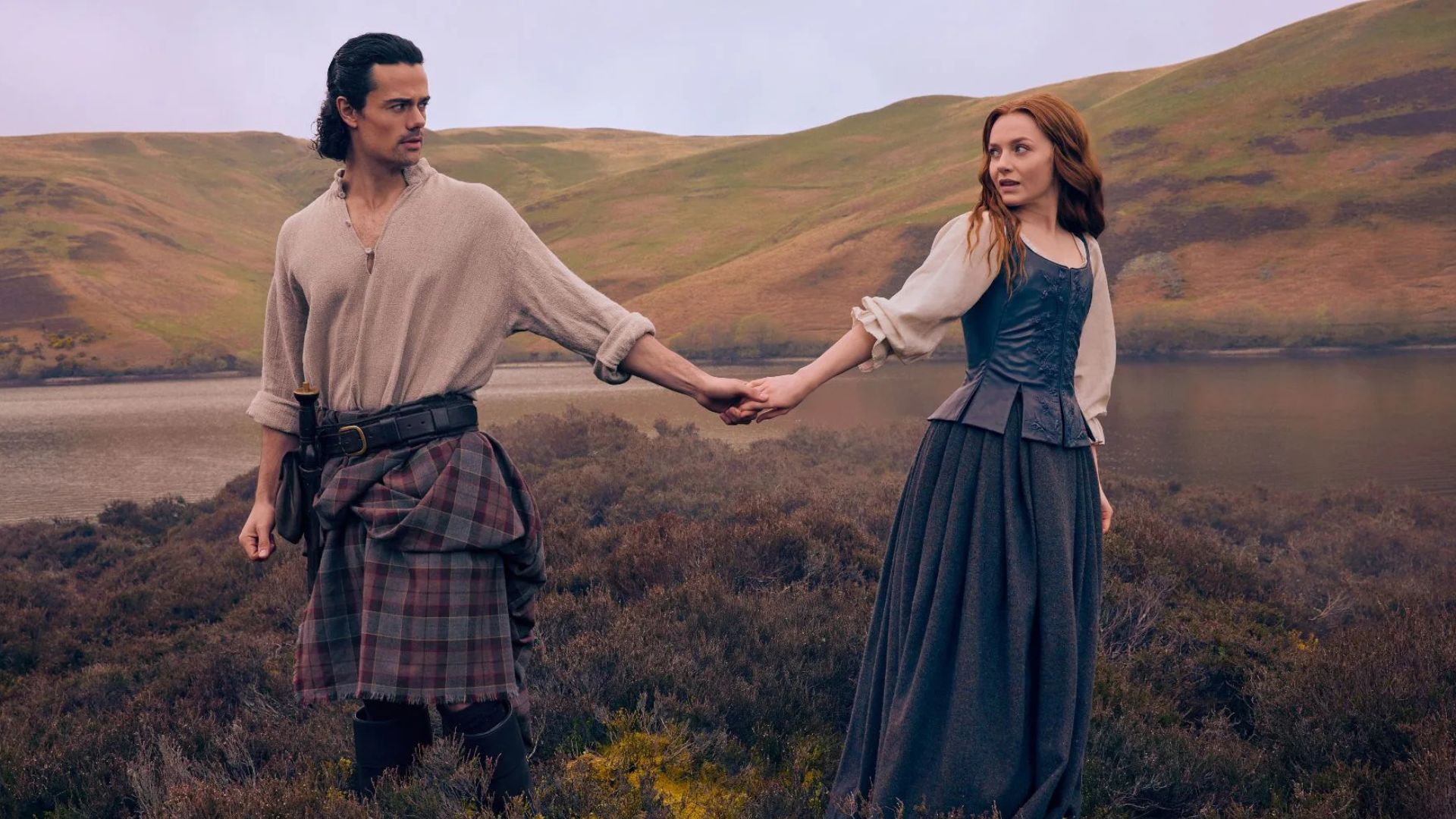 Brian and Ellen hold hands in a field.