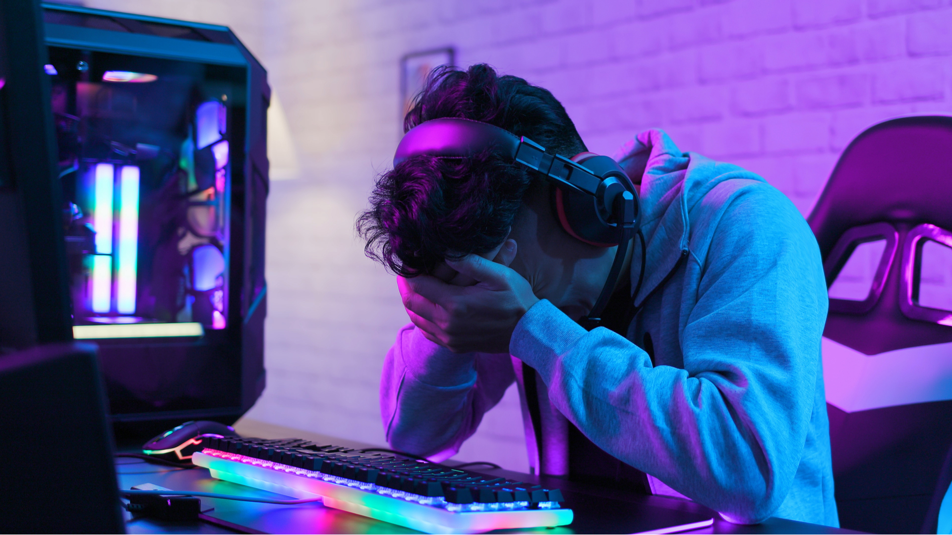 A sad looking person with his head in his hands sat in front of a gaming PC