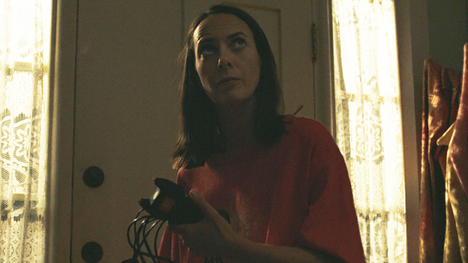 Patricia holding a stun gun and its charging cable in her house at night in episode 8 of Widow's Bay.