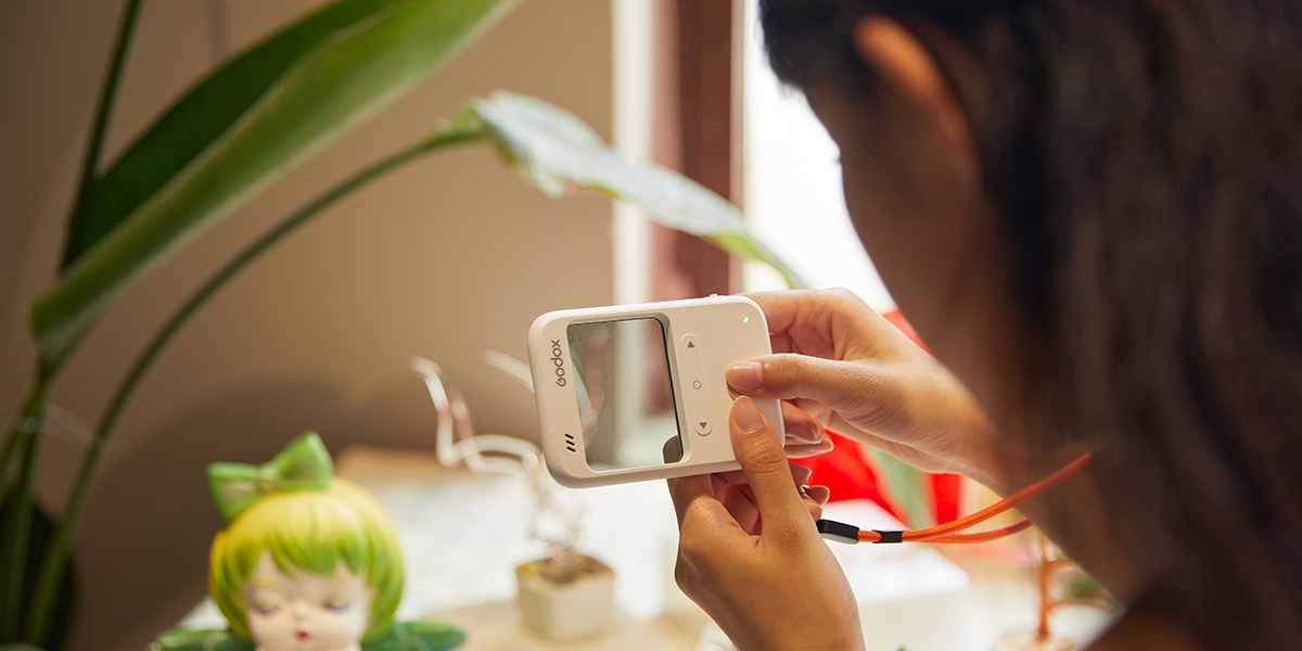 Woman holding a Godox C100 clear window camera and using it to take a photograph of a plastic doll