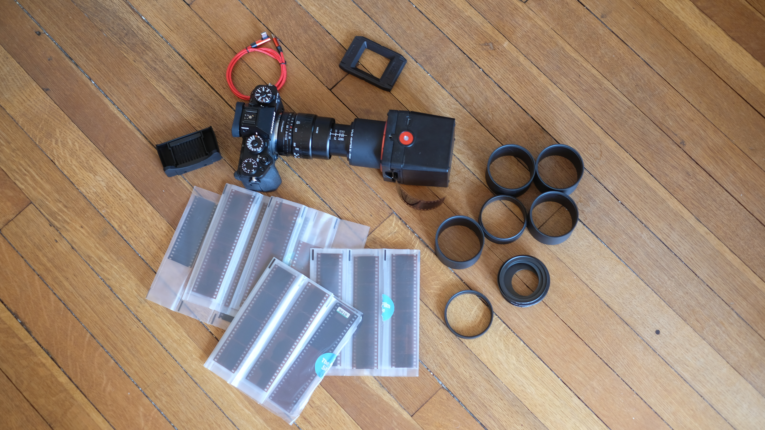 Photograph of Valoi Easy35 V2 film scanner kit placed on the floor, including camera, scanner, extension tubes, stand, brush, USB cable and film negatives.