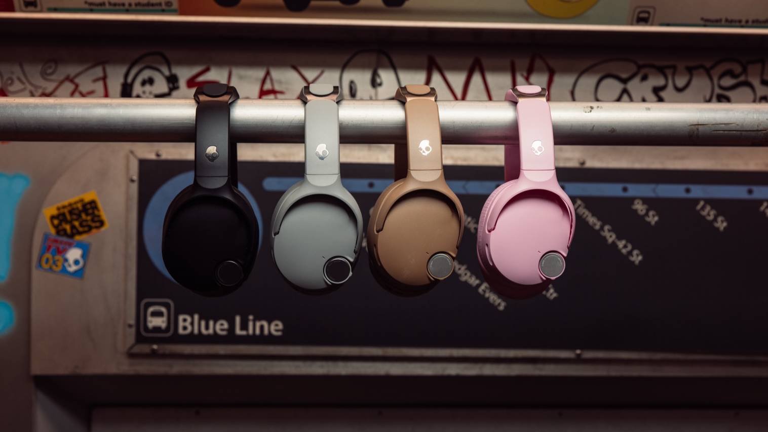 Four models of different colors of Skullcandy Crusher 1080, hanging on a subway bar.