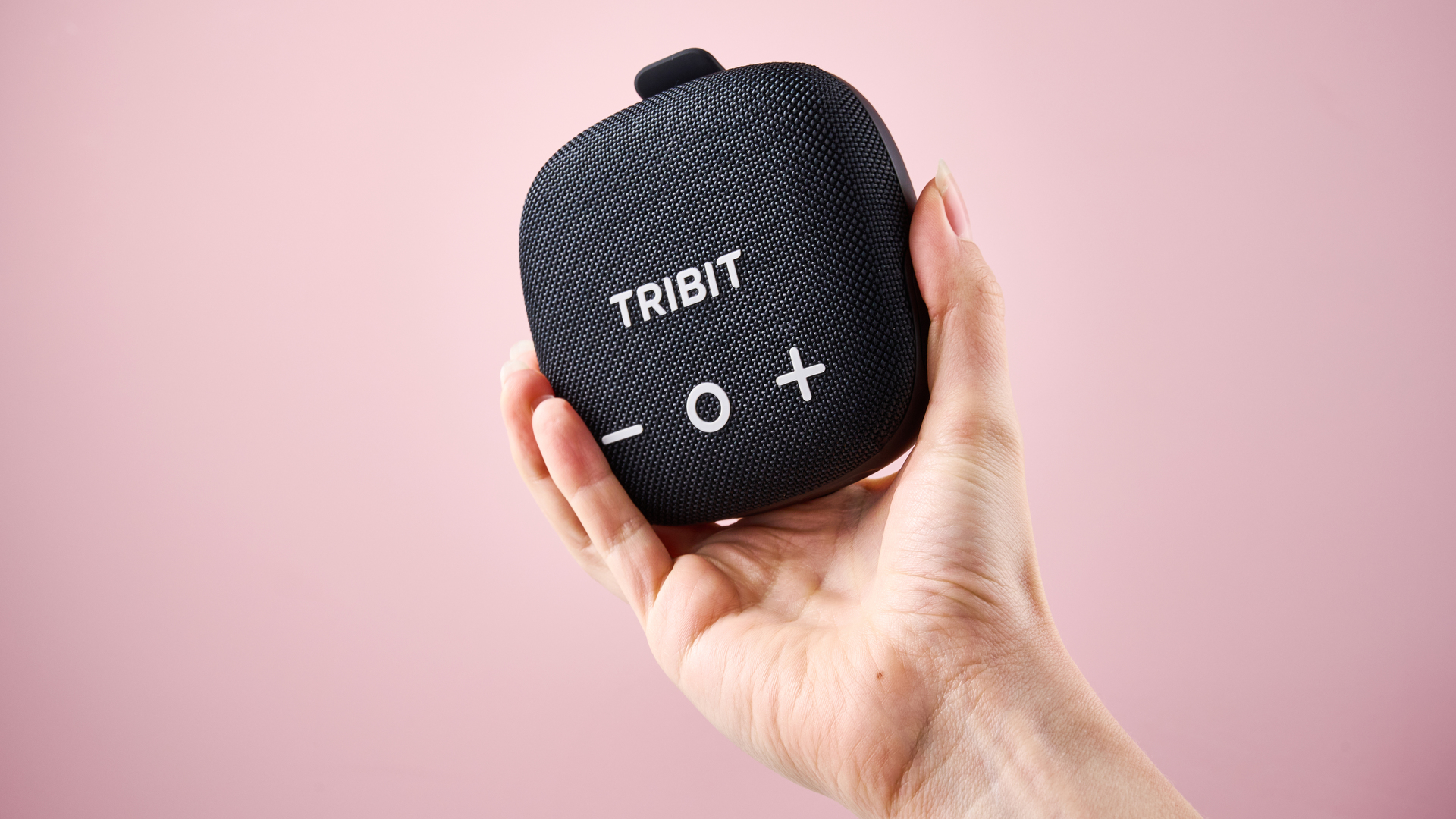 A woman's hand holding the Tribit Stormbox Micro 3 in front of a pink background.