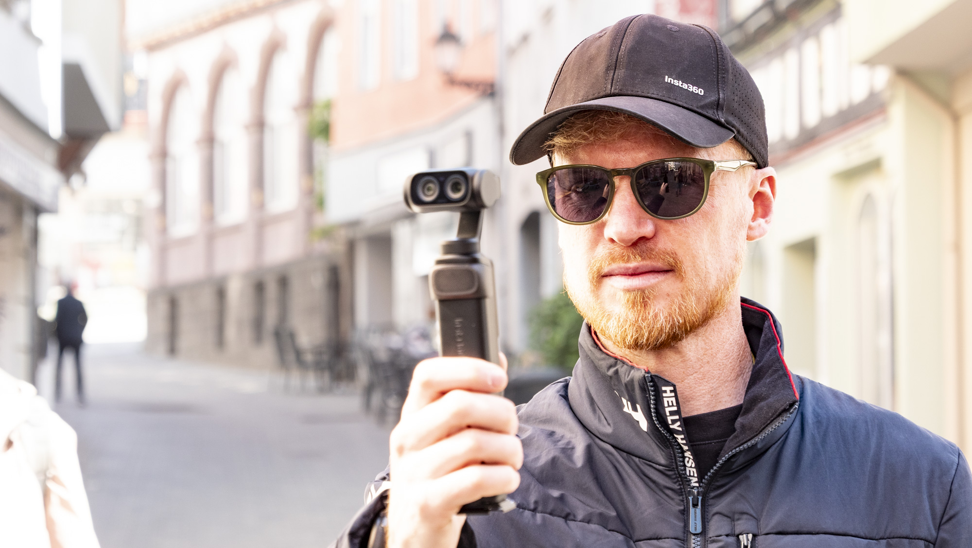 Man holding Insta360 Luna Ultra vlogging camera on a sunny day in an old town
