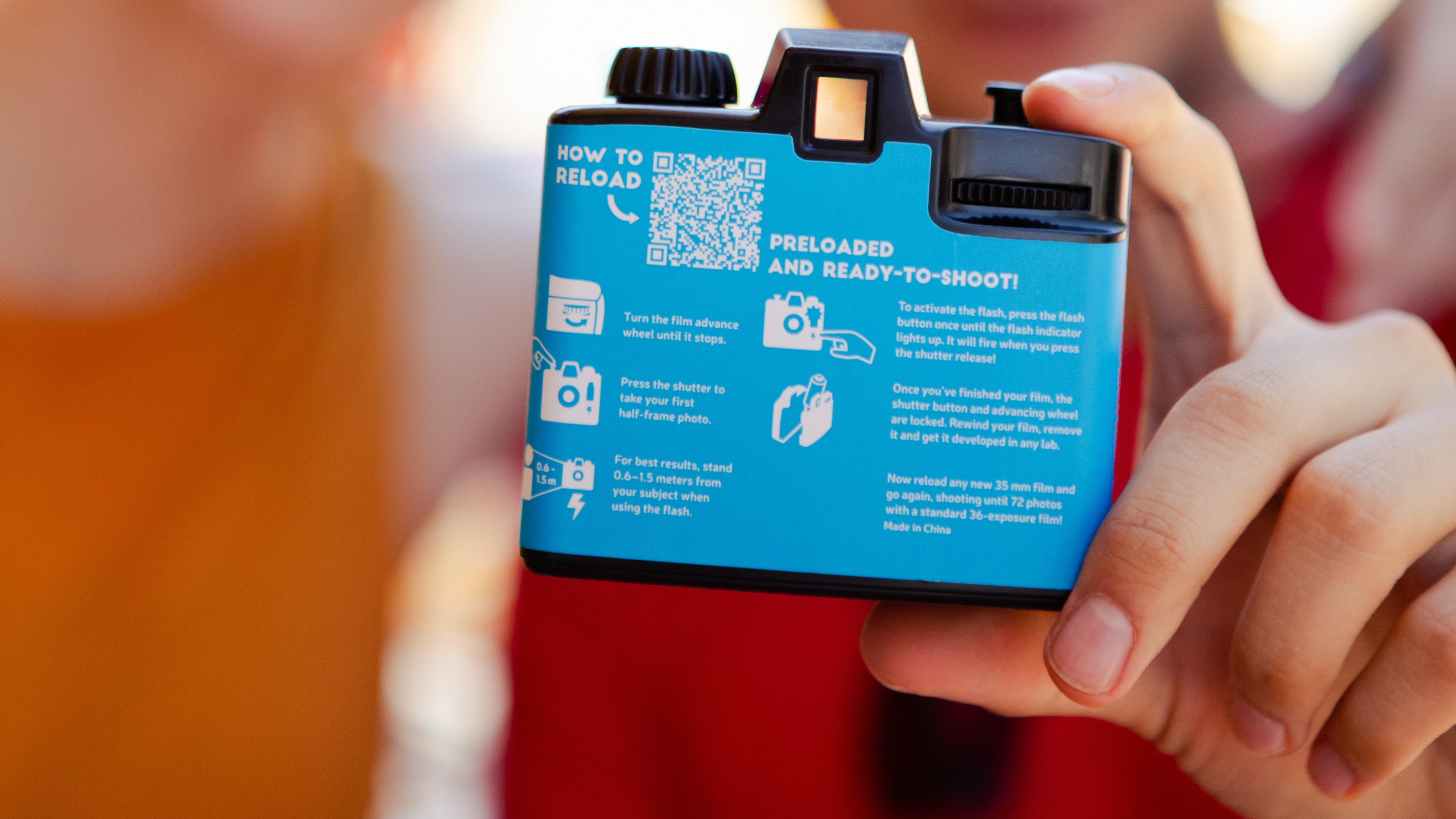 Photograph of a hand holding the Lomography half-frame easy-to-use rechargeable film camera, showing the back of the camera with written instructions, diagrams and a QR code.