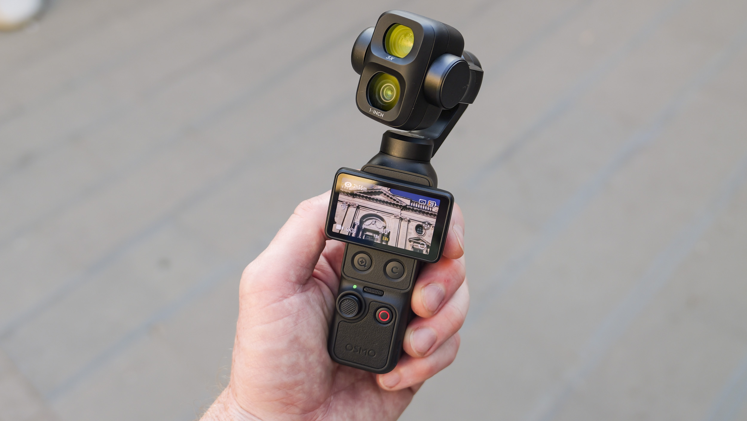 DJI Osmo Pocket 4P vlogging camera in a person's hand on a city street, screen rotated horizontally